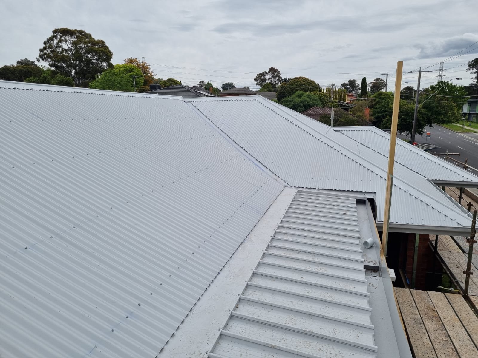 Metal roofing on a residential building with scaffolding and nearby trees and street.