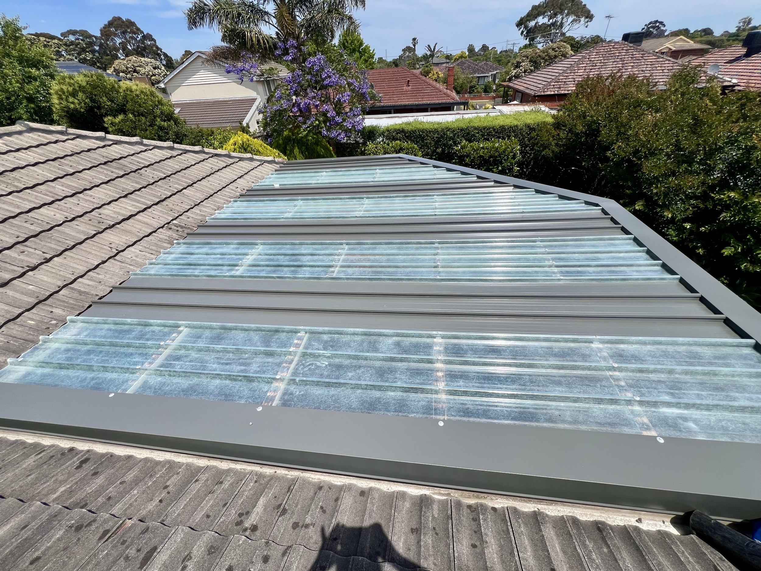 Roof with solar panels or skylights, surrounded by trees and neighboring houses.