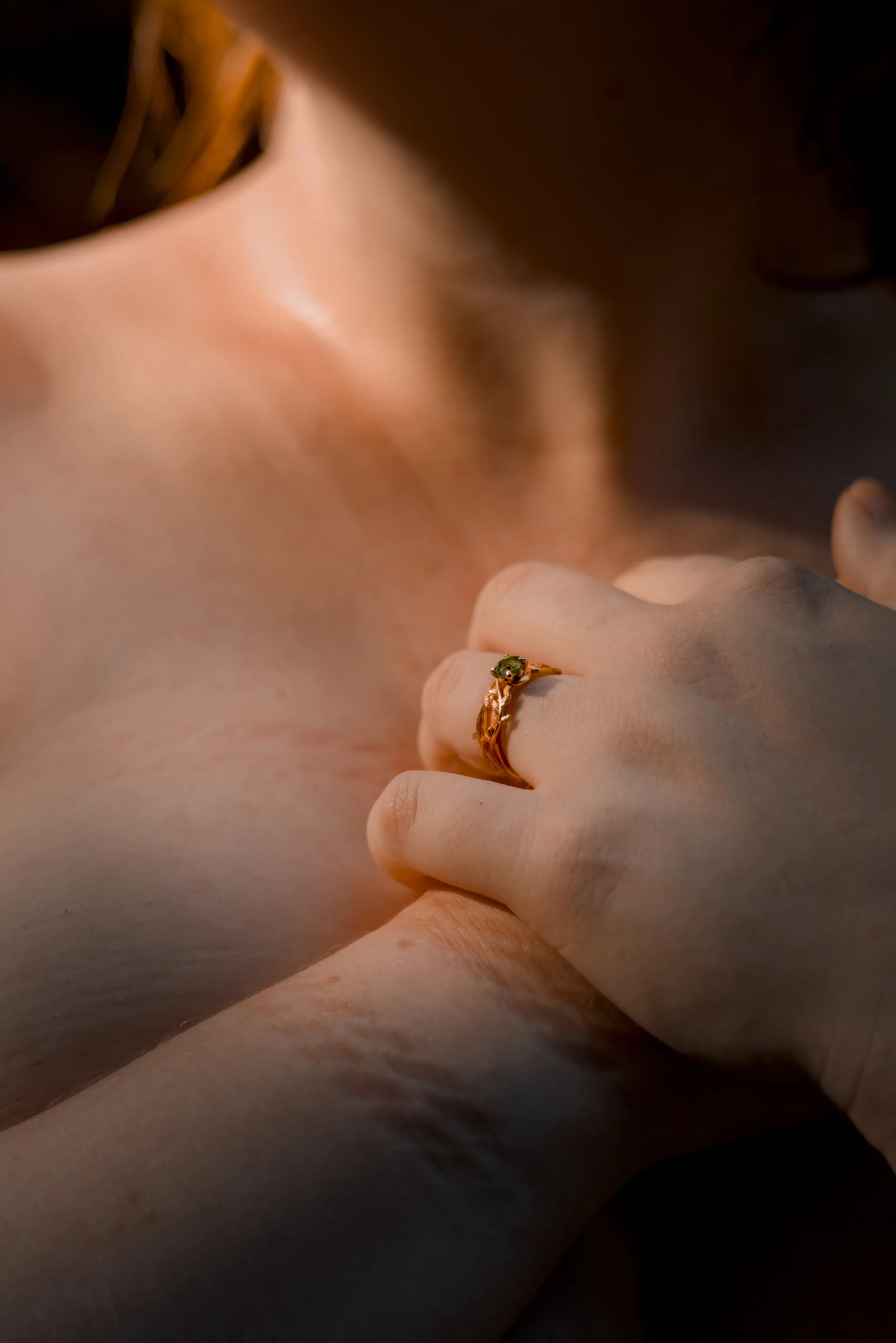 Close-up of a hand with an elegant rose gold ring featuring a green gemstone, resting on her chest.
