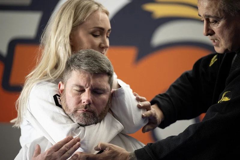 A man receiving a shoulder massage from two women in a martial arts training environment.