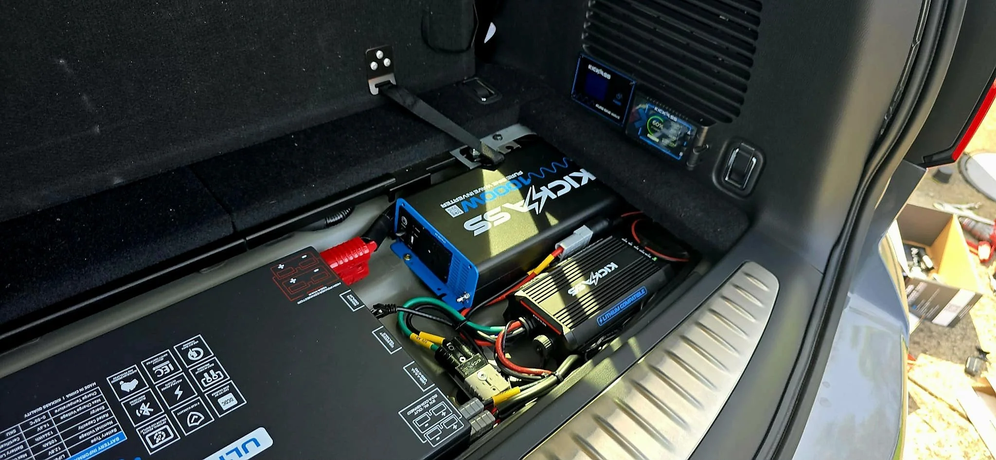 Inside the trunk of a vehicle with visible electronic equipment including a battery, wiring, and electronic modules.