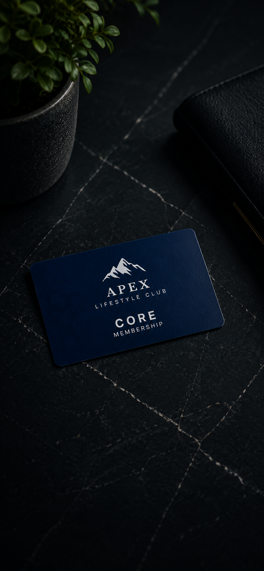 A dark blue Apex Lifestyle Club Core Membership card lies on a black marble surface, with a potted green plant and a black textured notebook nearby.