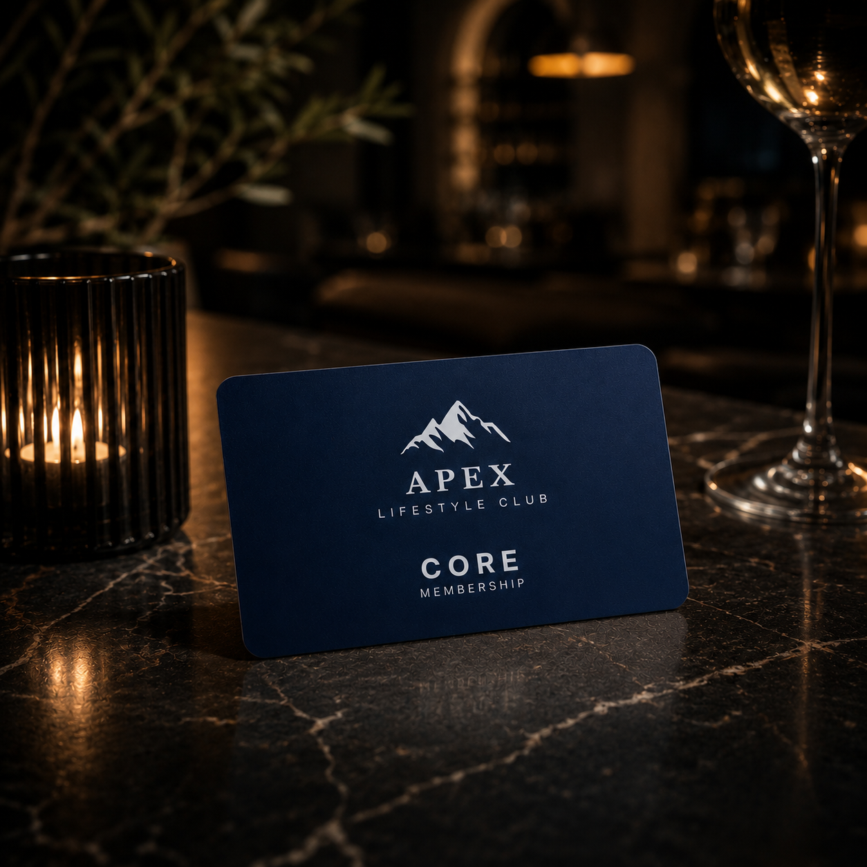 A navy blue card on a dark marble table with the logo and name 'Apex Lifestyle Club' and the words 'Core Membership'. Next to the card, there is a candle holder and a wine glass in a dimly lit setting.