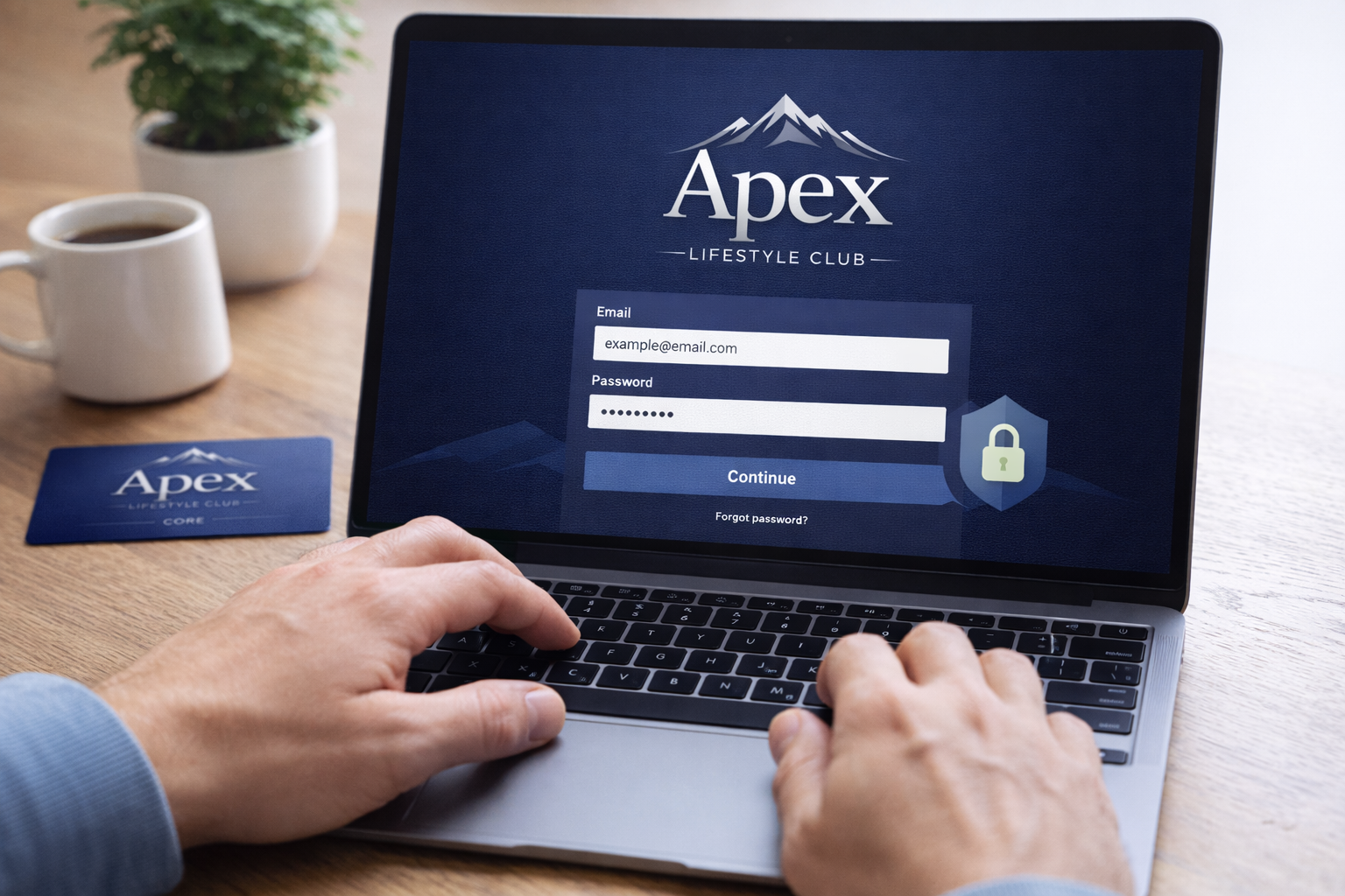 A person using a laptop to log into the Apex Lifestyle Club website, with a coffee mug, a potted plant, and a membership card on the wooden desk.