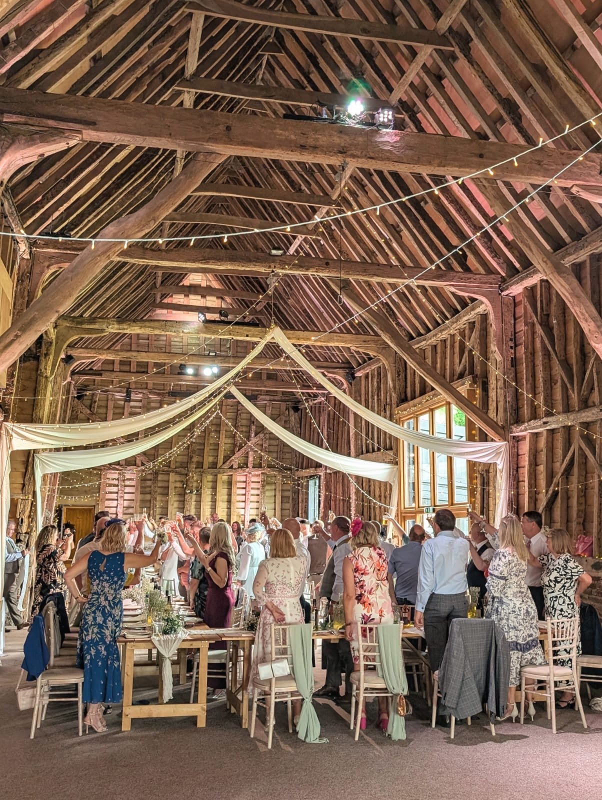 Wedding party standing to raise a glass to the bridge and groom, barn venue, Suffolk Barn Hawstead