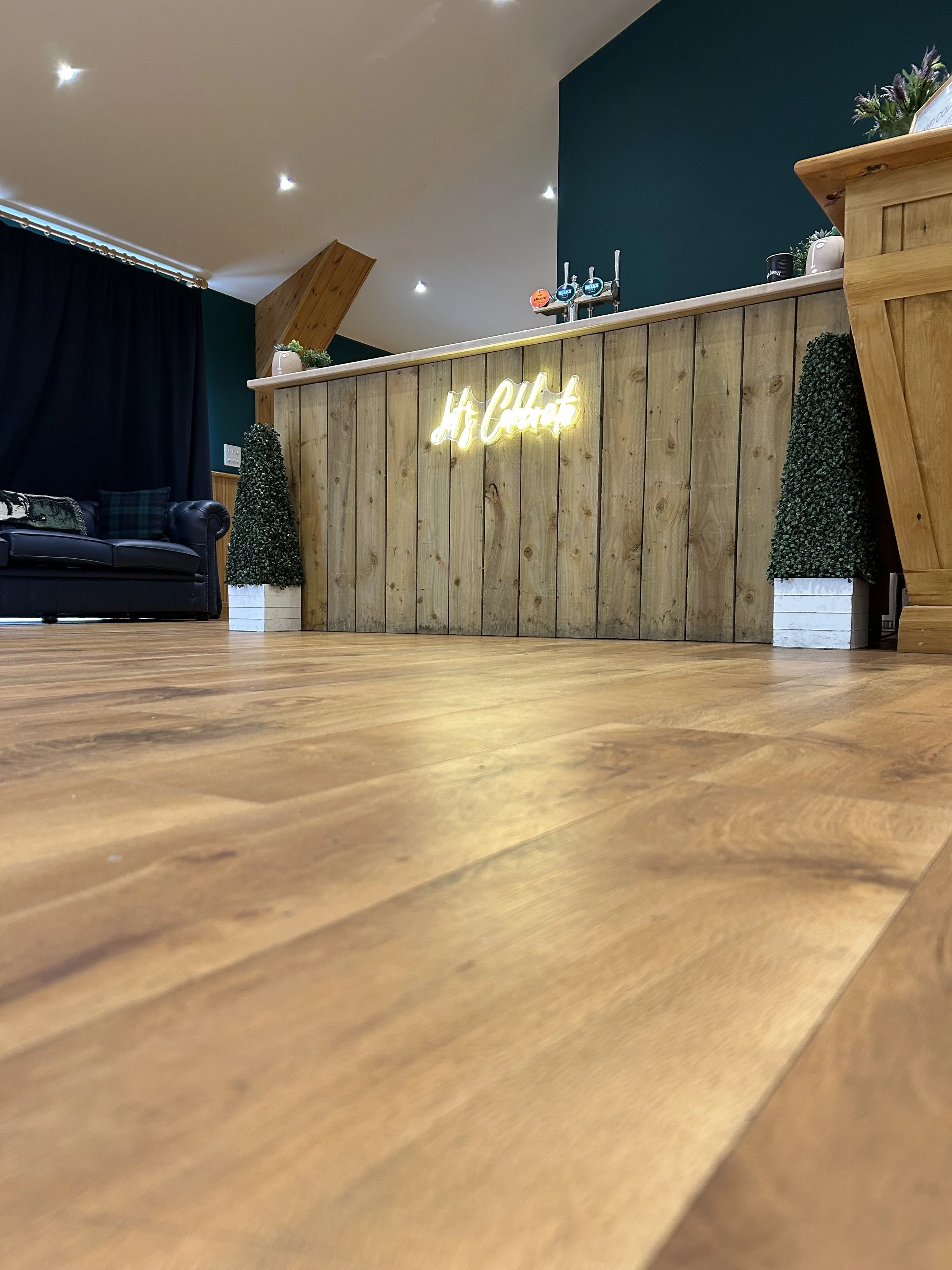 Rustic wooden bar, beer pumps, lets celebrate decrotive sign, prop decorotive trees at the bar corners and bar top plants