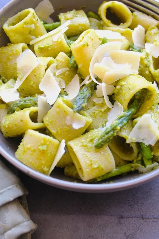Pasta salad with large rigatoni pasta, green asparagus pieces, and shavings of white cheese in a bowl.