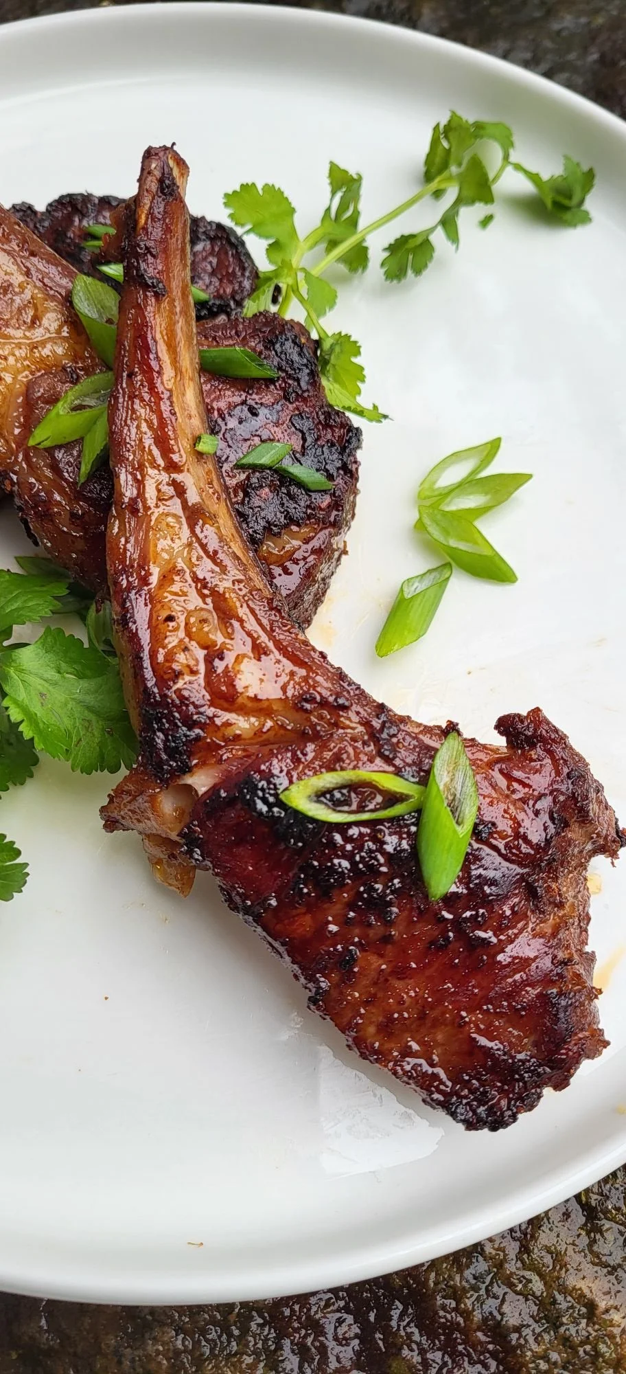 Close-up of a grilled lamb chop garnished with green onions and cilantro on a white plate.