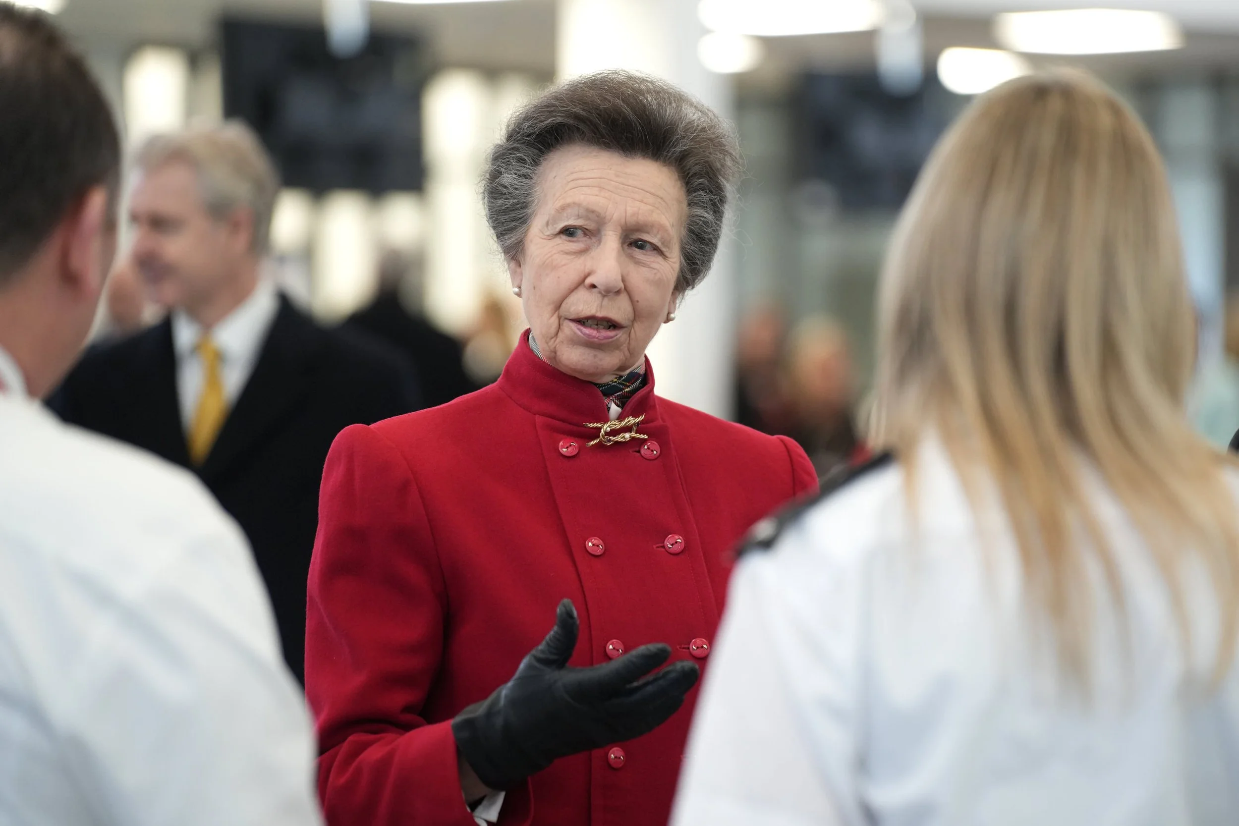 Anne, Princess Royal in a red jacket and black gloves is speaking to two people, one in a white uniform and another with blonde hair at the Fire Training Centre, Oxfordshire.