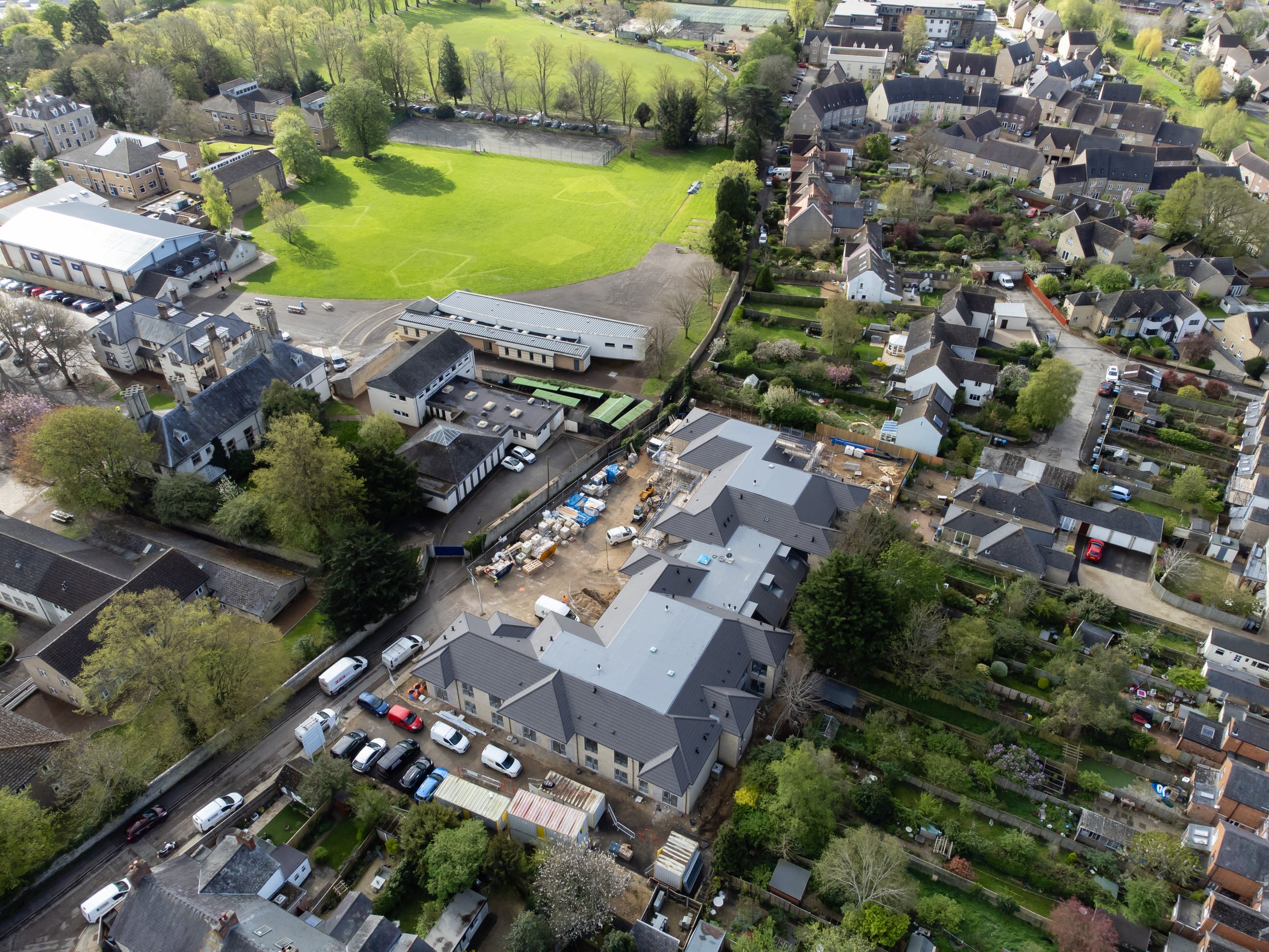 An aerial view of a residential neighborhood showing houses, gardens, a school, and a sports field.