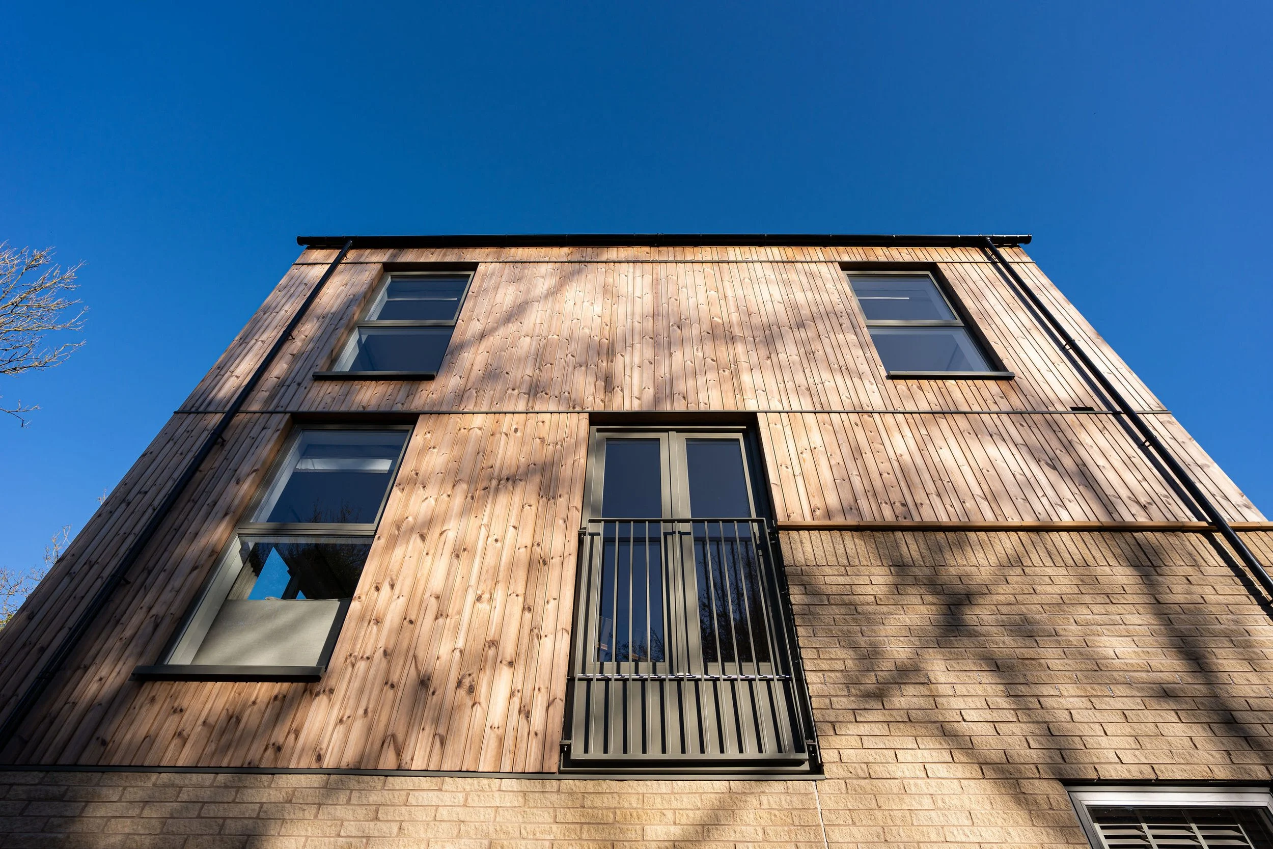 Low angle view of a modern multi-story building with wooden siding and large glass windows against a clear blue sky.