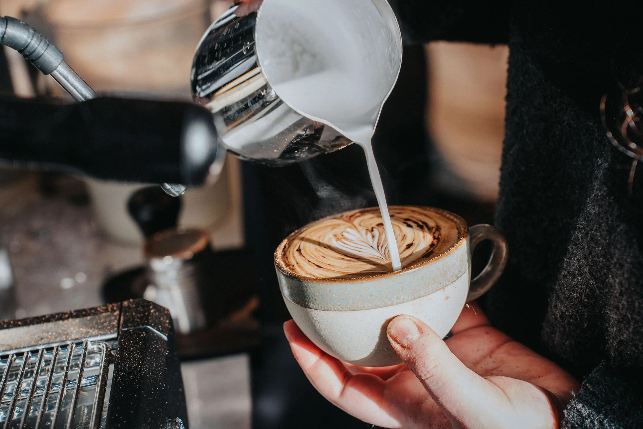 Barista pours steamed milk into a cup of espresso, creating latte art in a coffee shop.