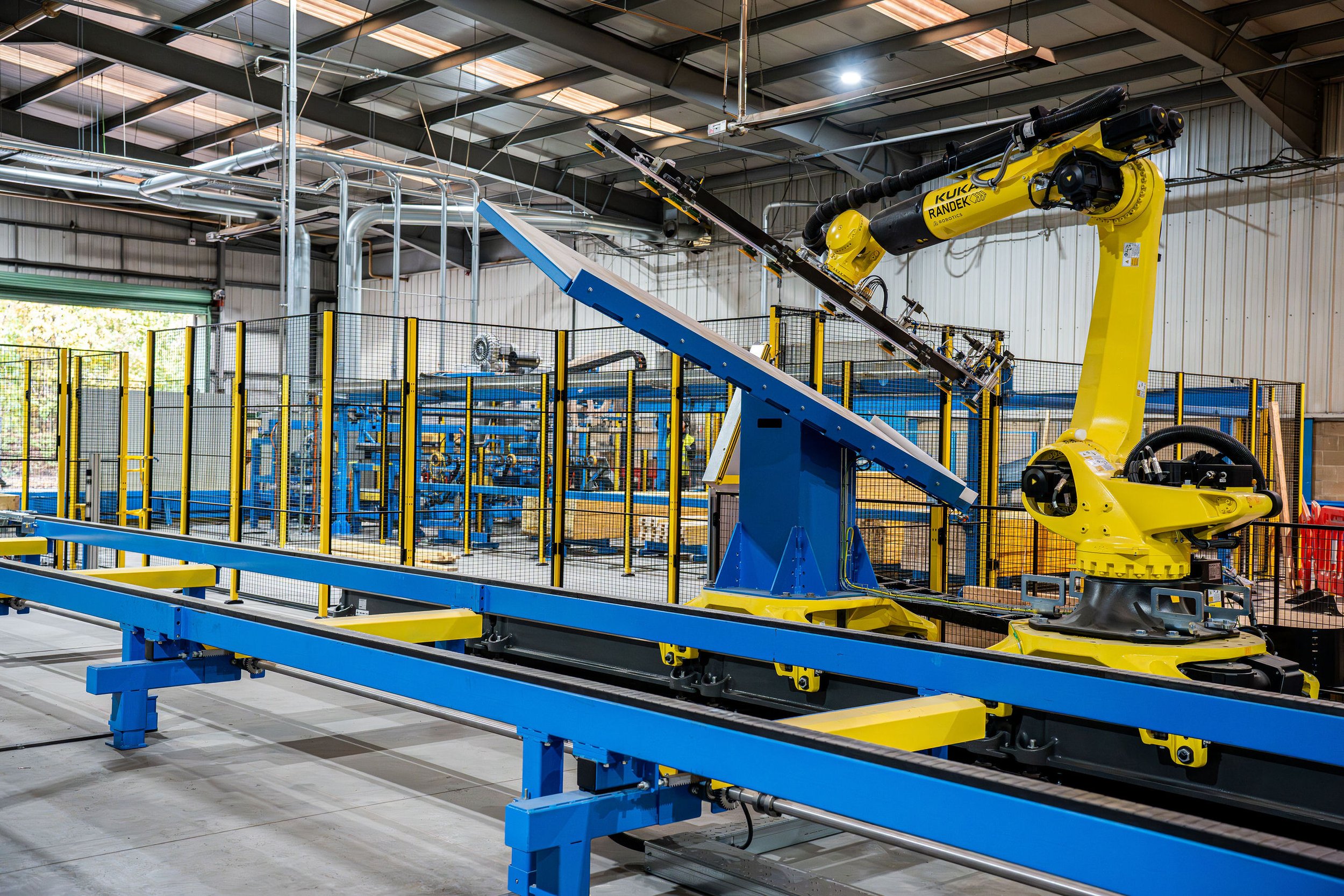 Industrial robot arm working inside a manufacturing facility with yellow and blue machinery.
