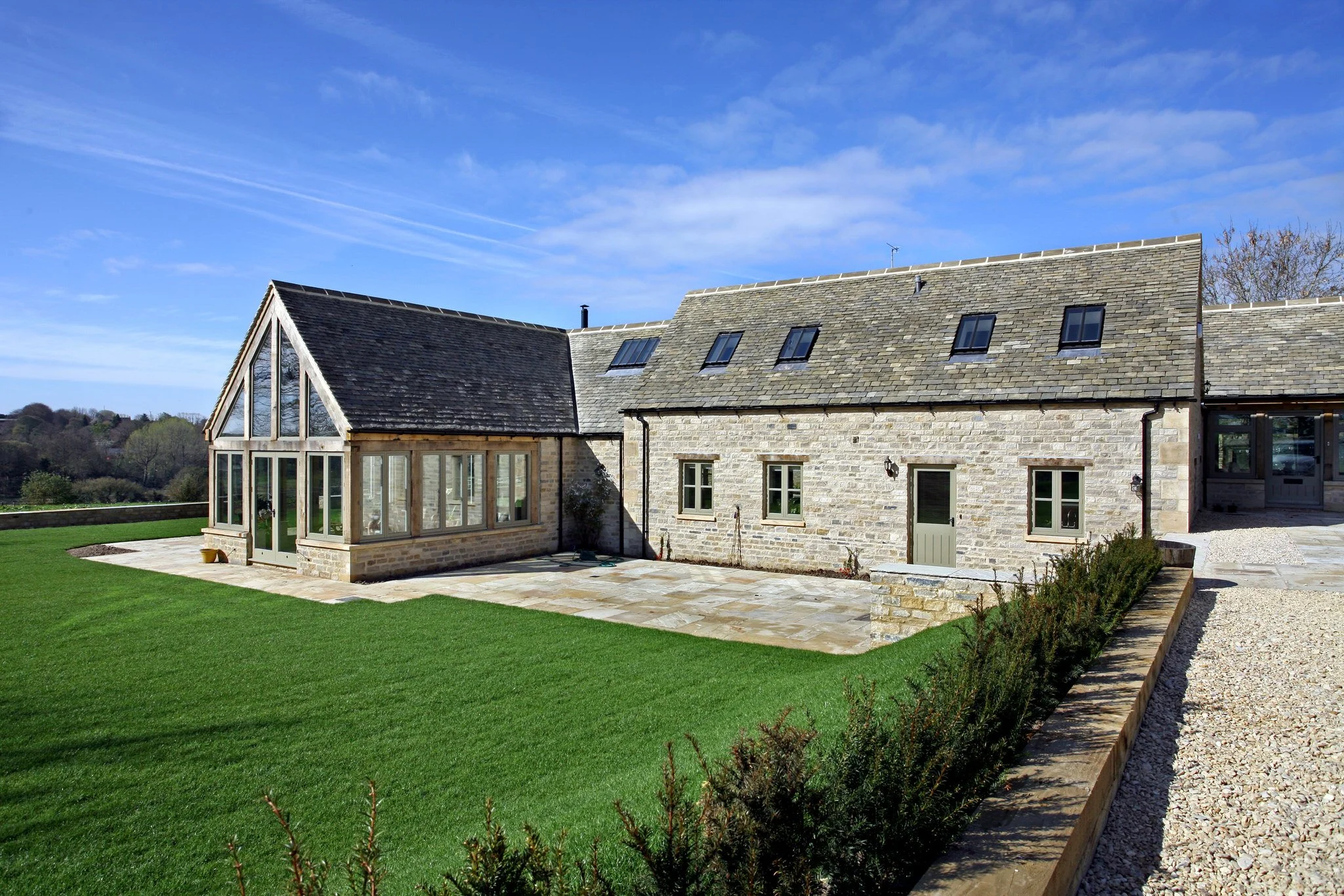 Stone house with a glass enclosed porch, green lawn, and a gravel pathway under a blue sky.