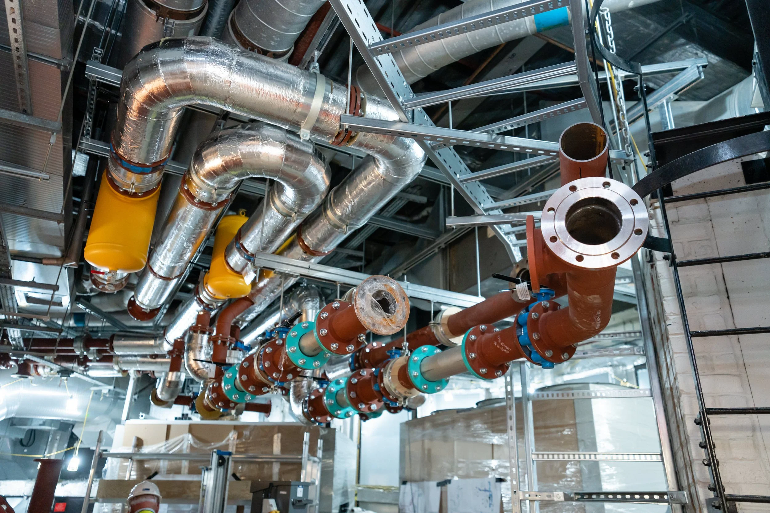 Underground industrial piping system with large metal pipes, insulated pipes, and valves in a construction site.