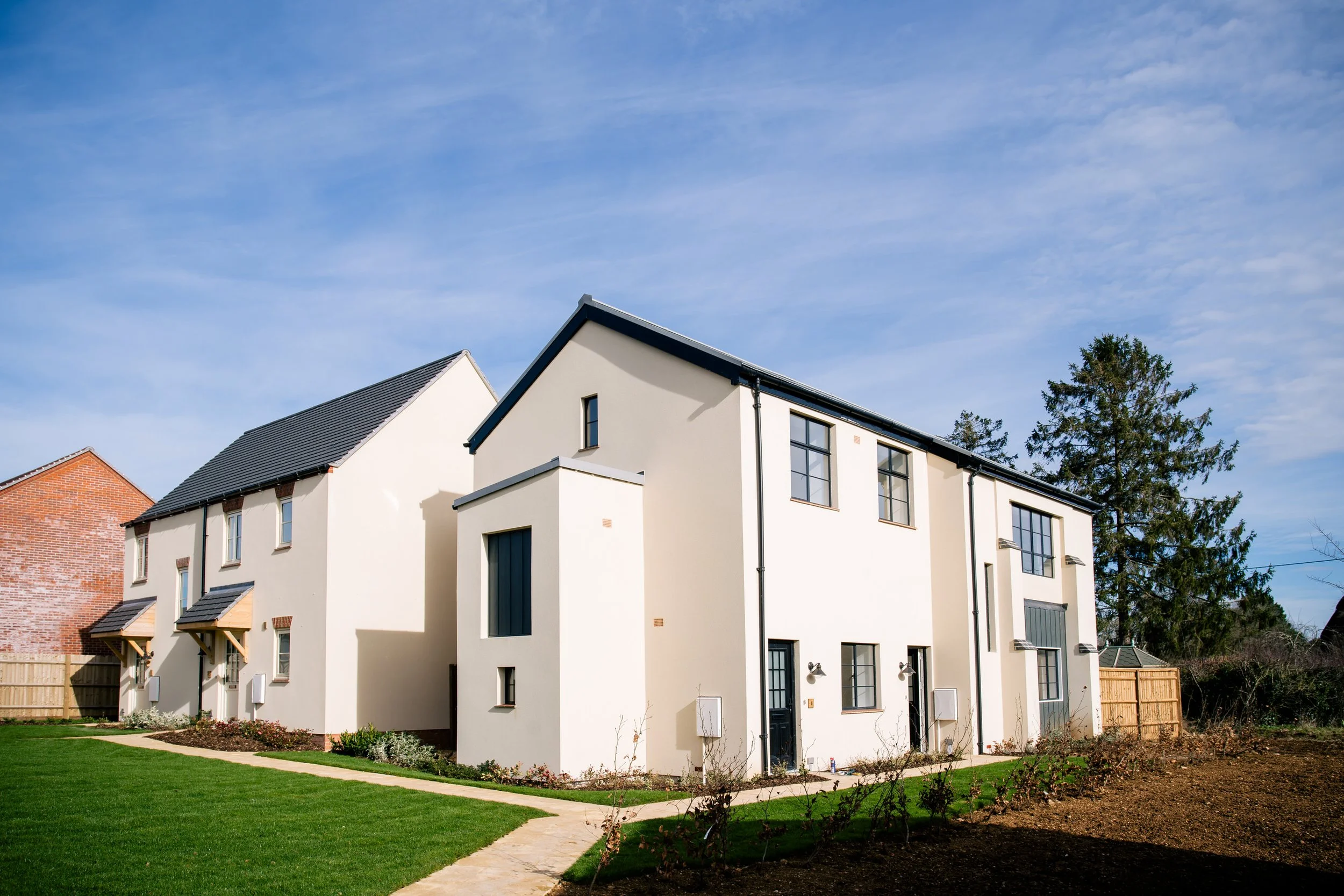 Modern white residential building with black roof lines and black window frames, surrounded by a lush green lawn and a clear blue sky.