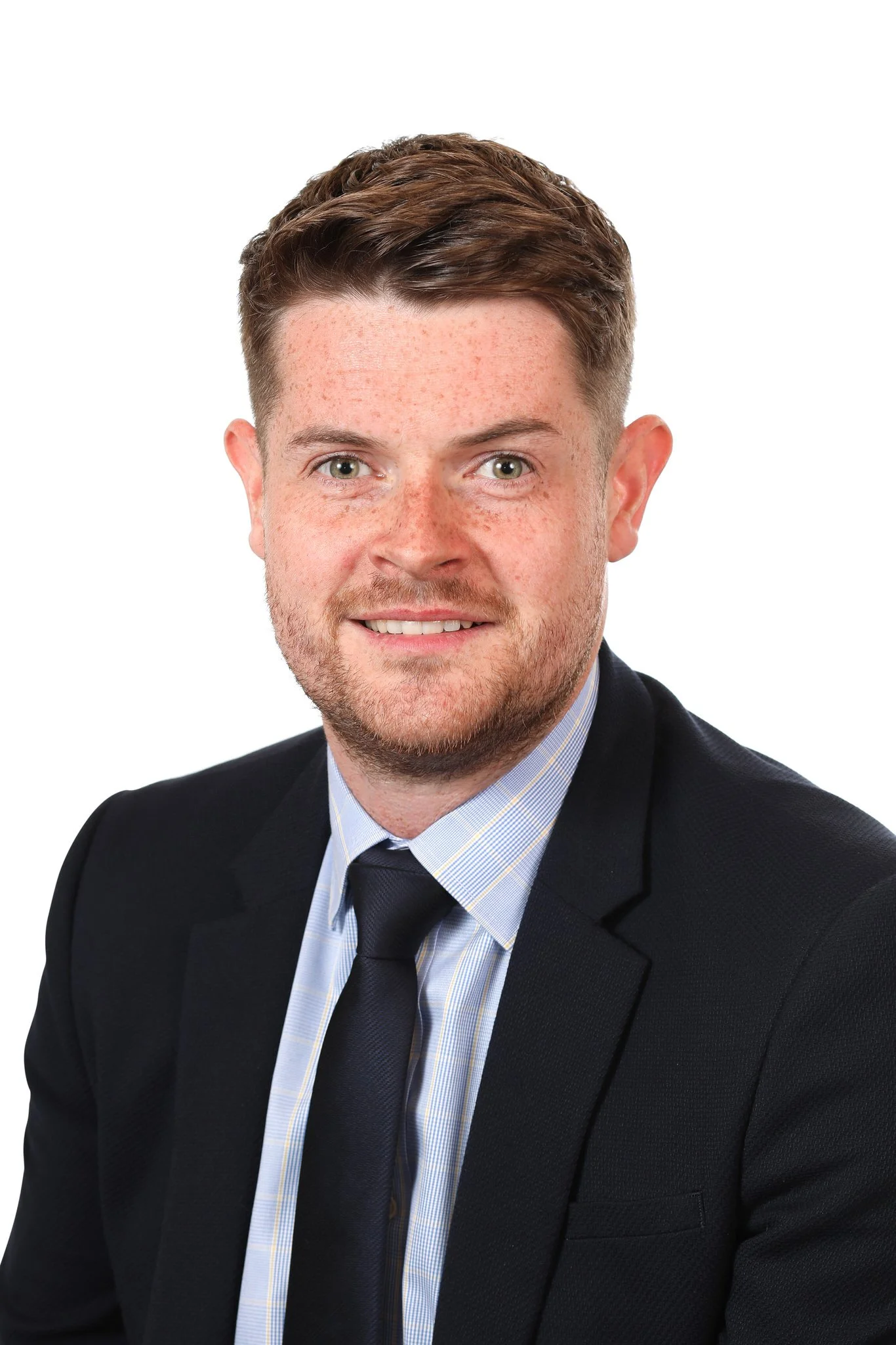 Headshot of a young man with brown hair, light skin, and freckles, wearing a dark suit, light blue shirt, and dark tie, against a white background.