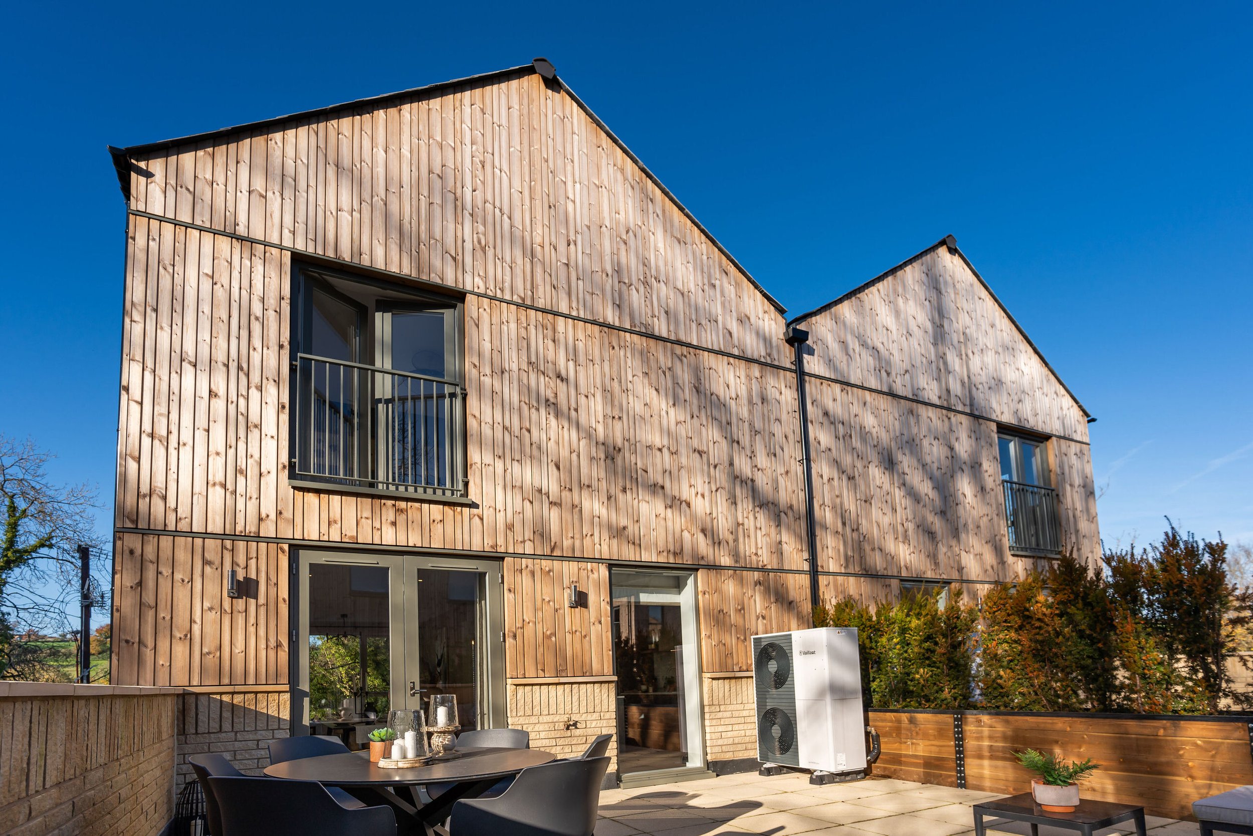 Modern wooden townhouse with balcony and patio furniture on a sunny day.