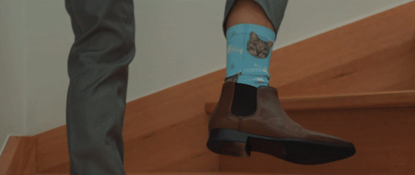 A person walking up wooden stairs wearing blue socks with a bear design and brown shoes.