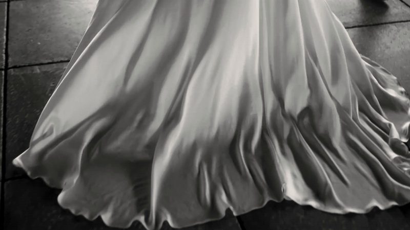 Close-up of a flowing, satin-like fabric in a ball gown or dress, with ruched detailing at the hem.