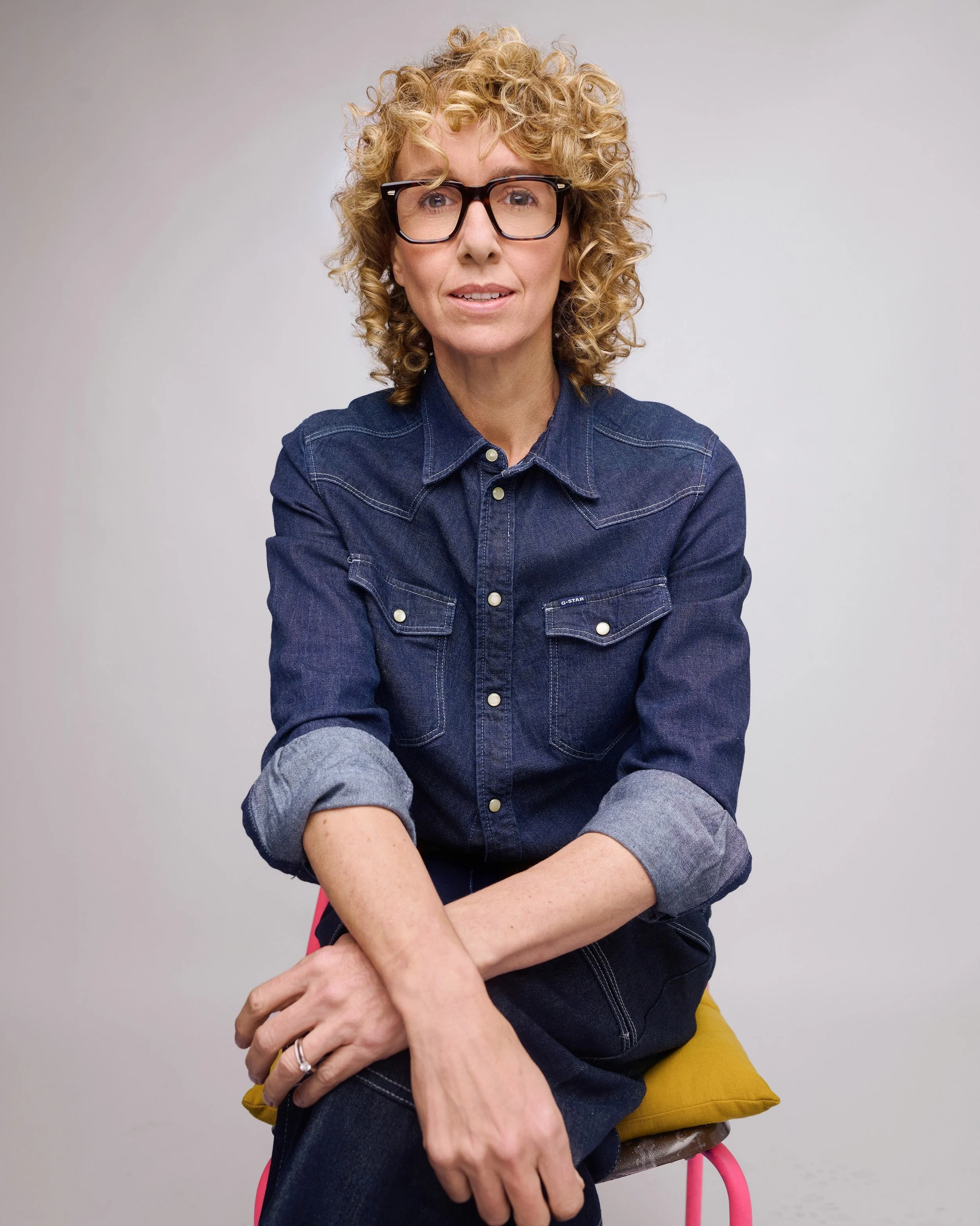 Rebecca Lewis seated in a denim shirt against a light grey backdrop