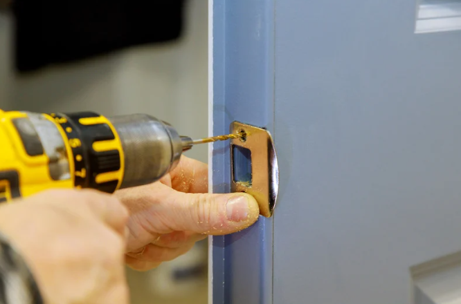 A person using a yellow cordless drill to install a lock on a blue door.