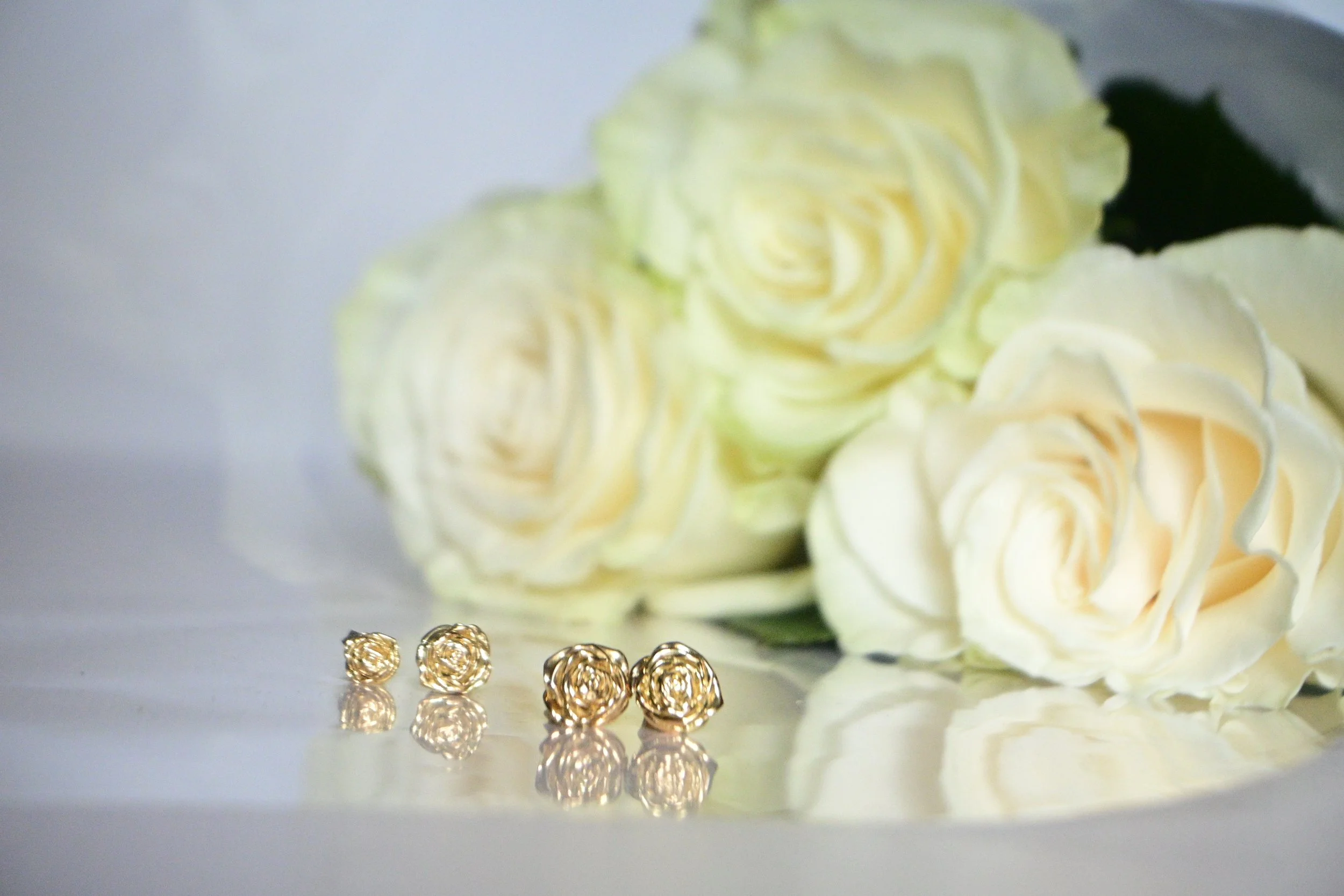 White rose's highlighting 18k gold rose earrings arranged in a row, showing size options on white linen.