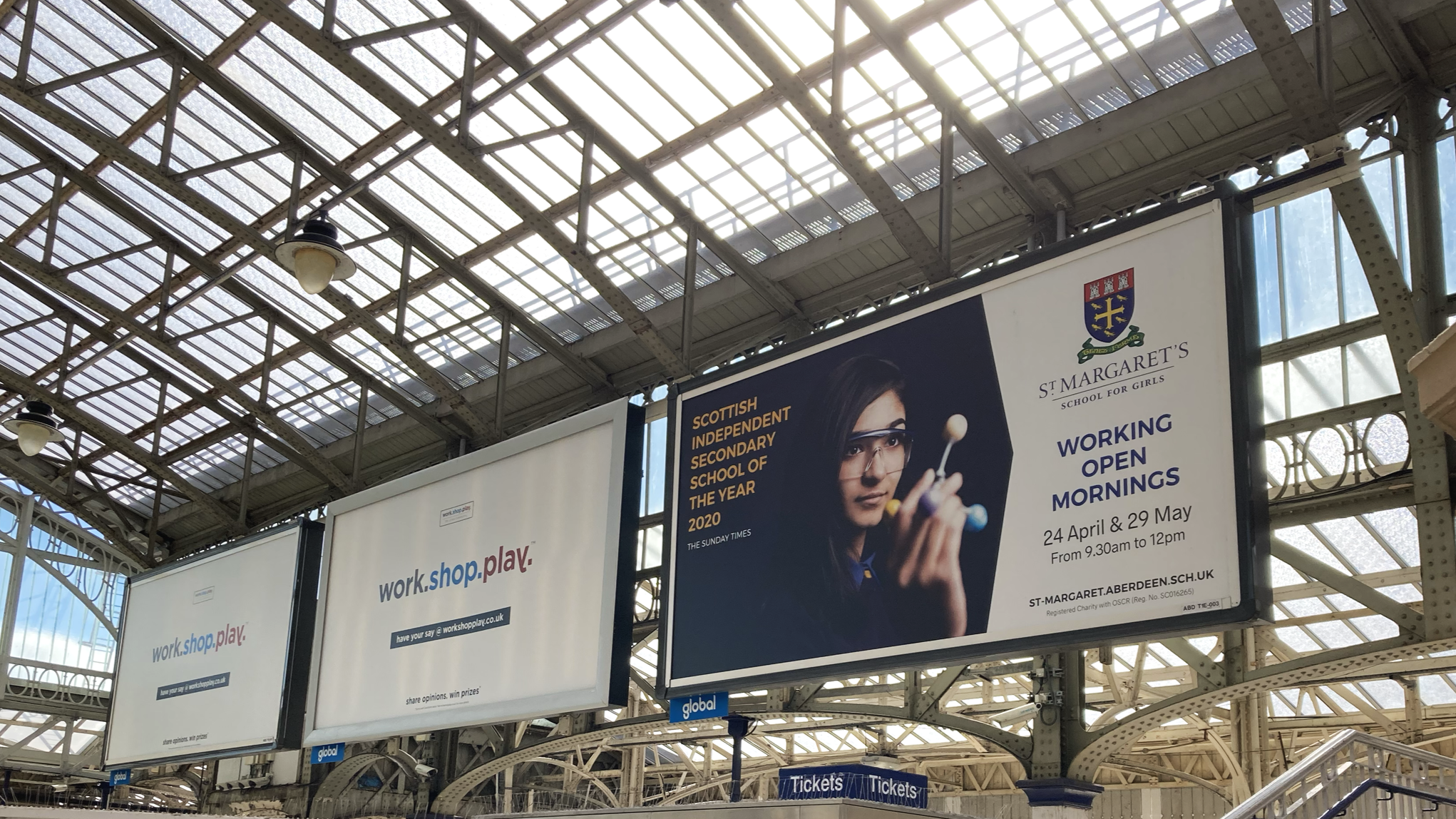 Advertisement banners at a train station: one promoting work, shop, and play, and the other for St. Margaret's School for Girls, highlighting their open mornings on April 24 and May 29.