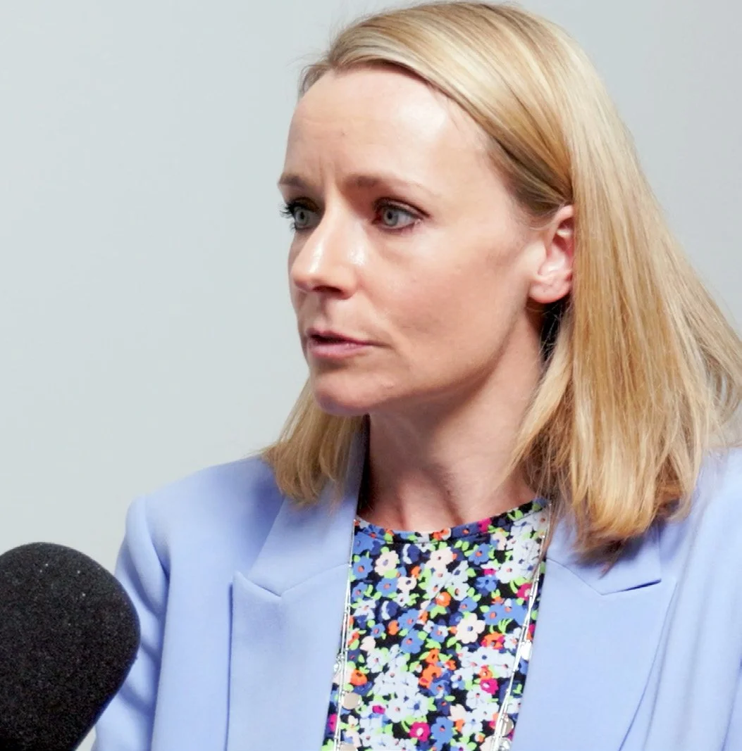 A woman with blonde hair speaking into a microphone during an interview or press conference.