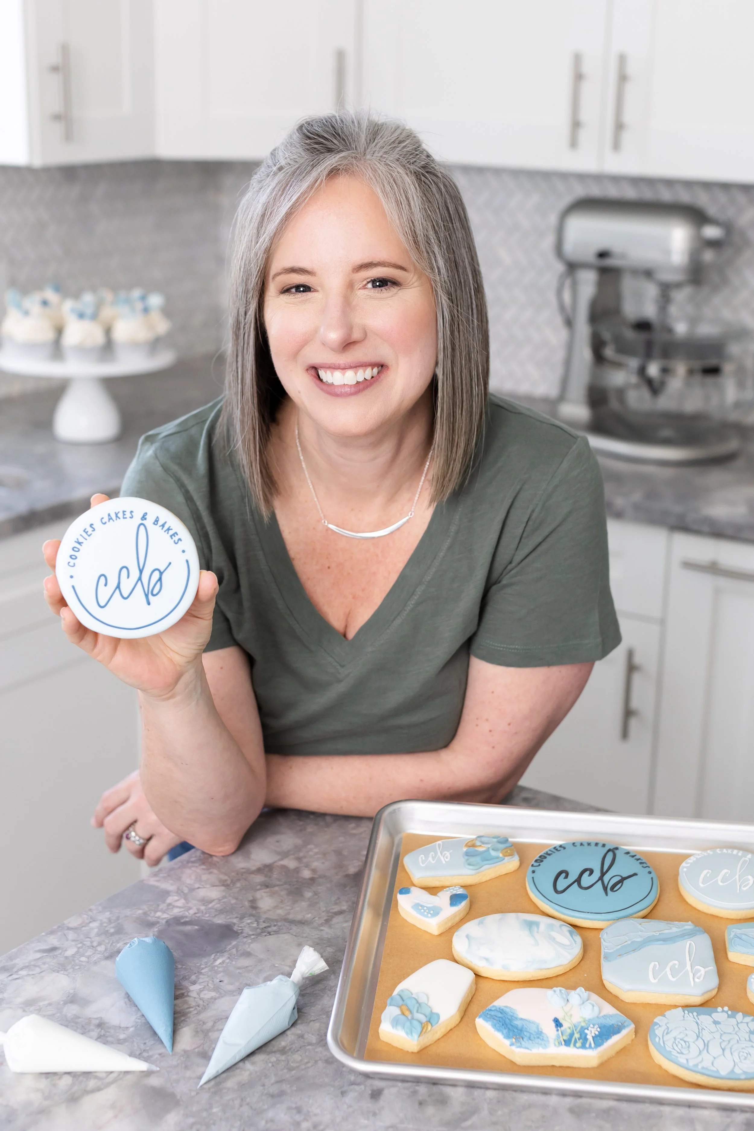 Smiling woman holding a sugar cookie with circle logo for Cookies Cakes & Bakes.