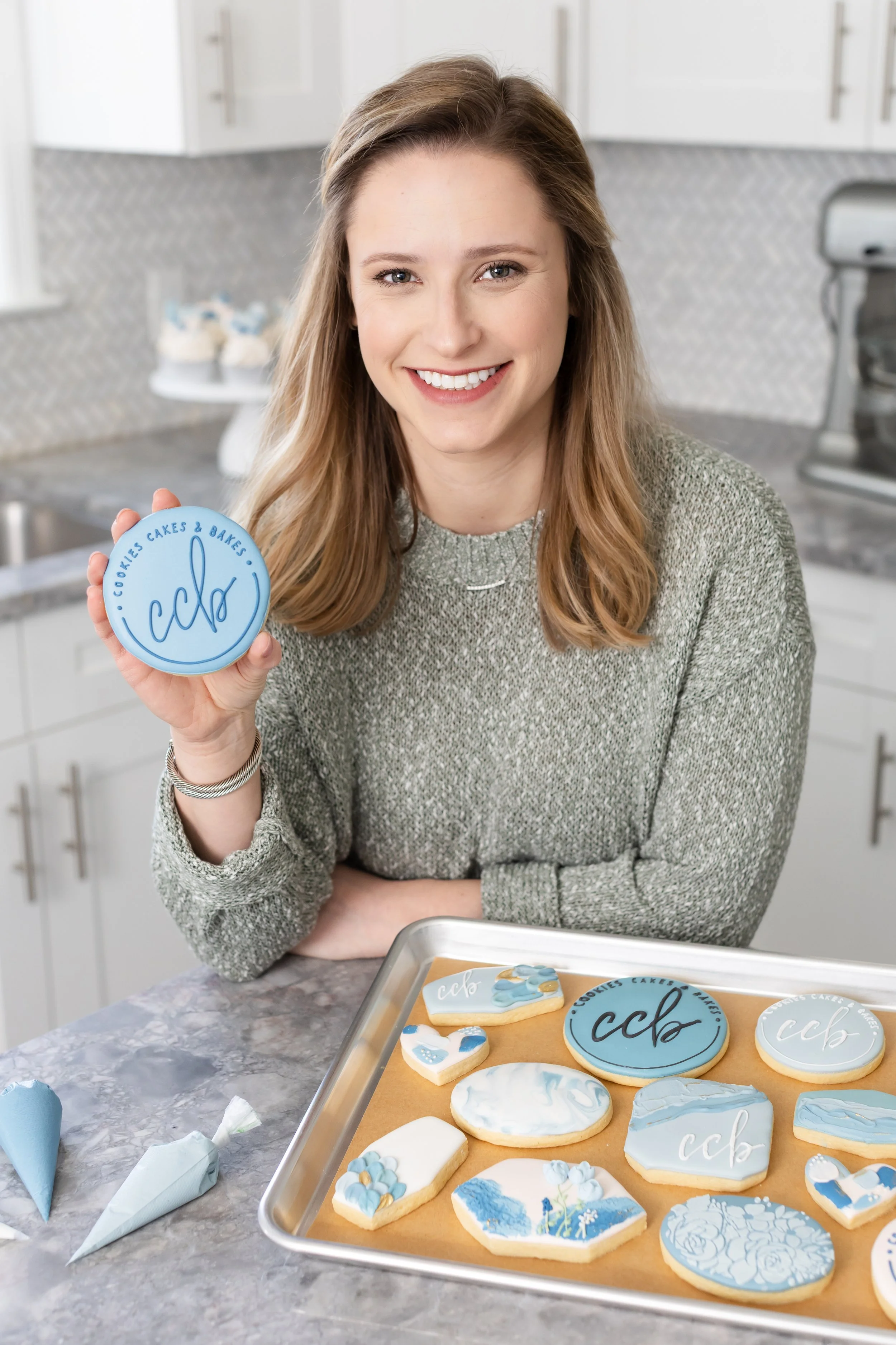Smiling woman holding a sugar cookie with circle logo for Cookies Cakes & Bakes.