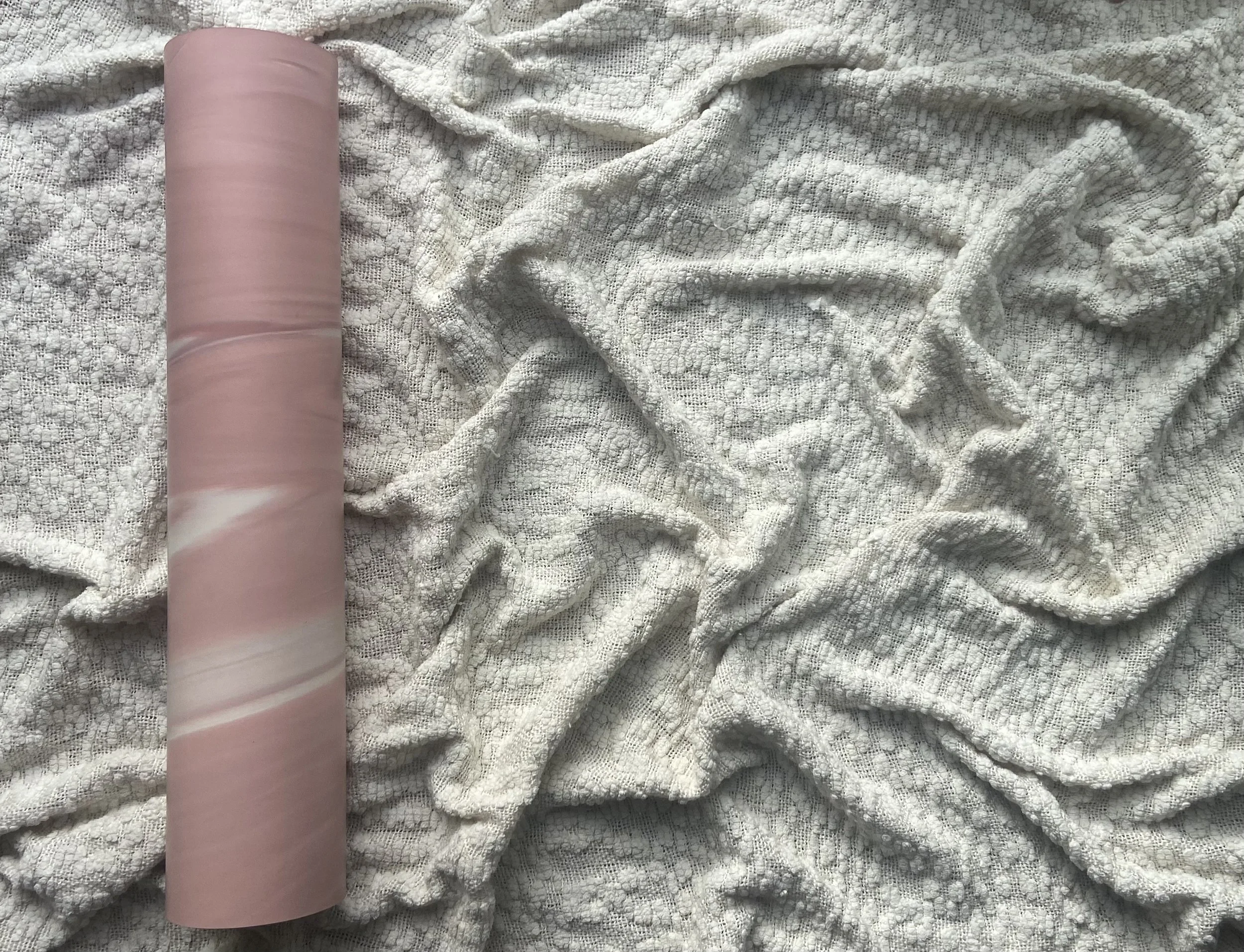 A roll of pink and white marbled wrapping paper on a white textured blanket.