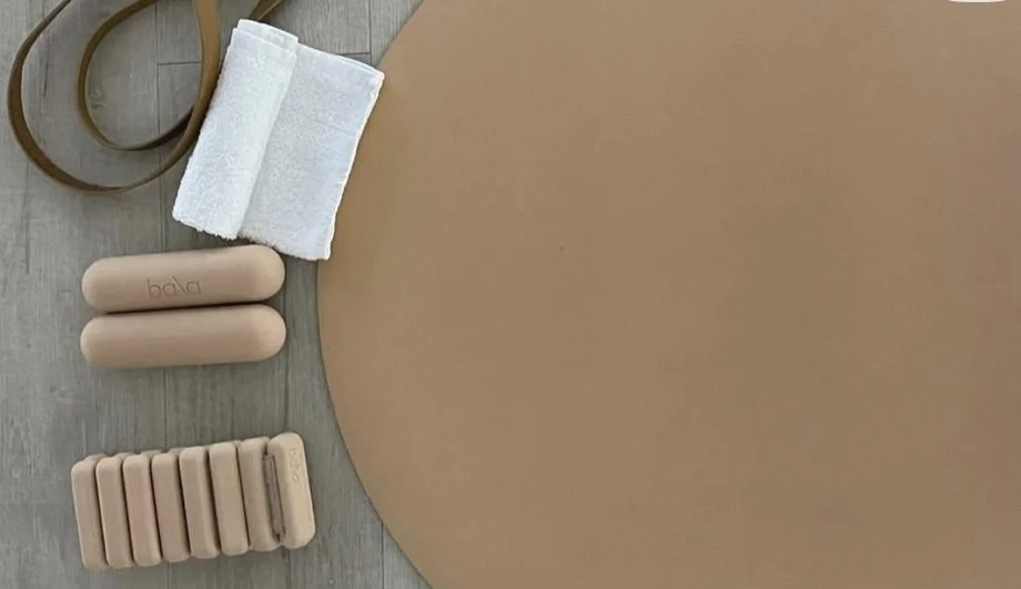 Flat lay of personal care items including two rolled white towels, two beige bottles labeled 'bala', a container with multiple beige tablets, and a brown elastic band on a wooden surface next to a large round brown object.