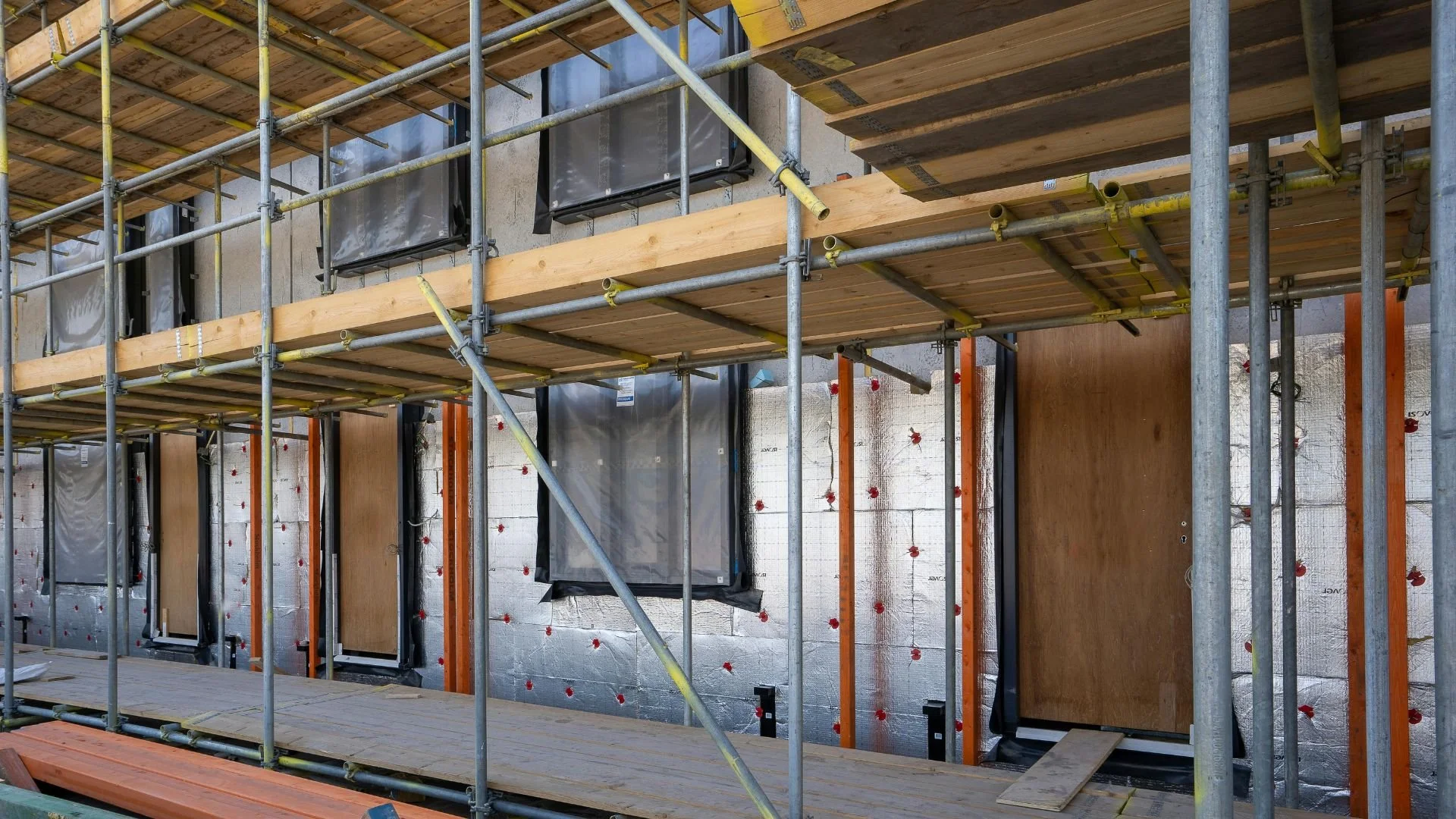 Construction site with scaffolding, plywood, and insulation on a building wall