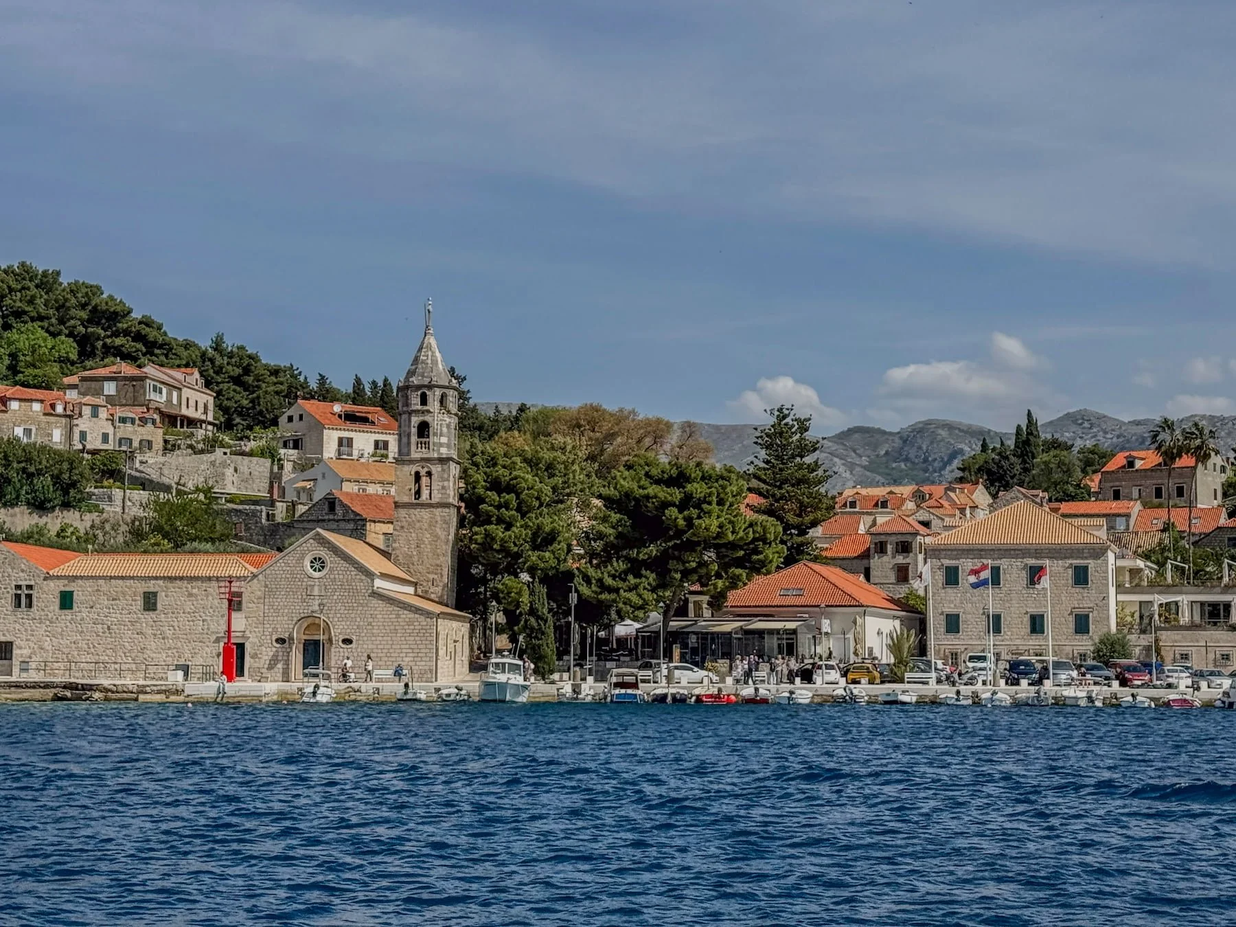 Cavtat waterfront seen from the ferry, with church bell tower and limestone mountains beyond.