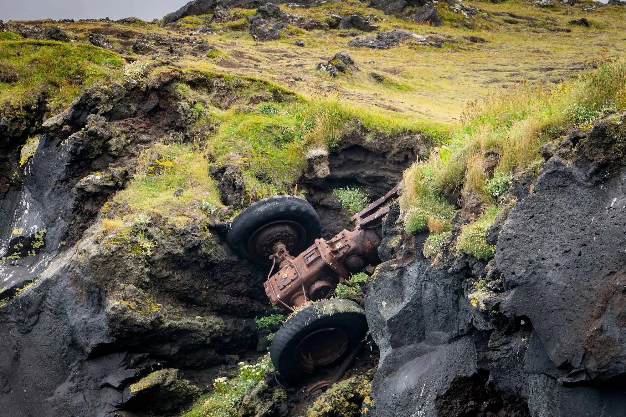Rusting remains of an old tractor wedged among volcanic rocks near the puffin cliffs on Vestmannaeyjar.