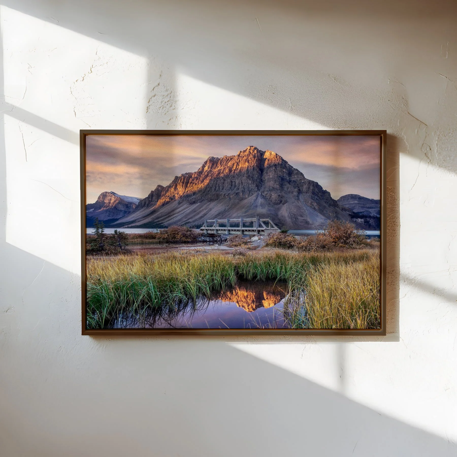 Bow Lake at Dawn metal print with a slim dark frame on a textured wall with sunlight and shadows.