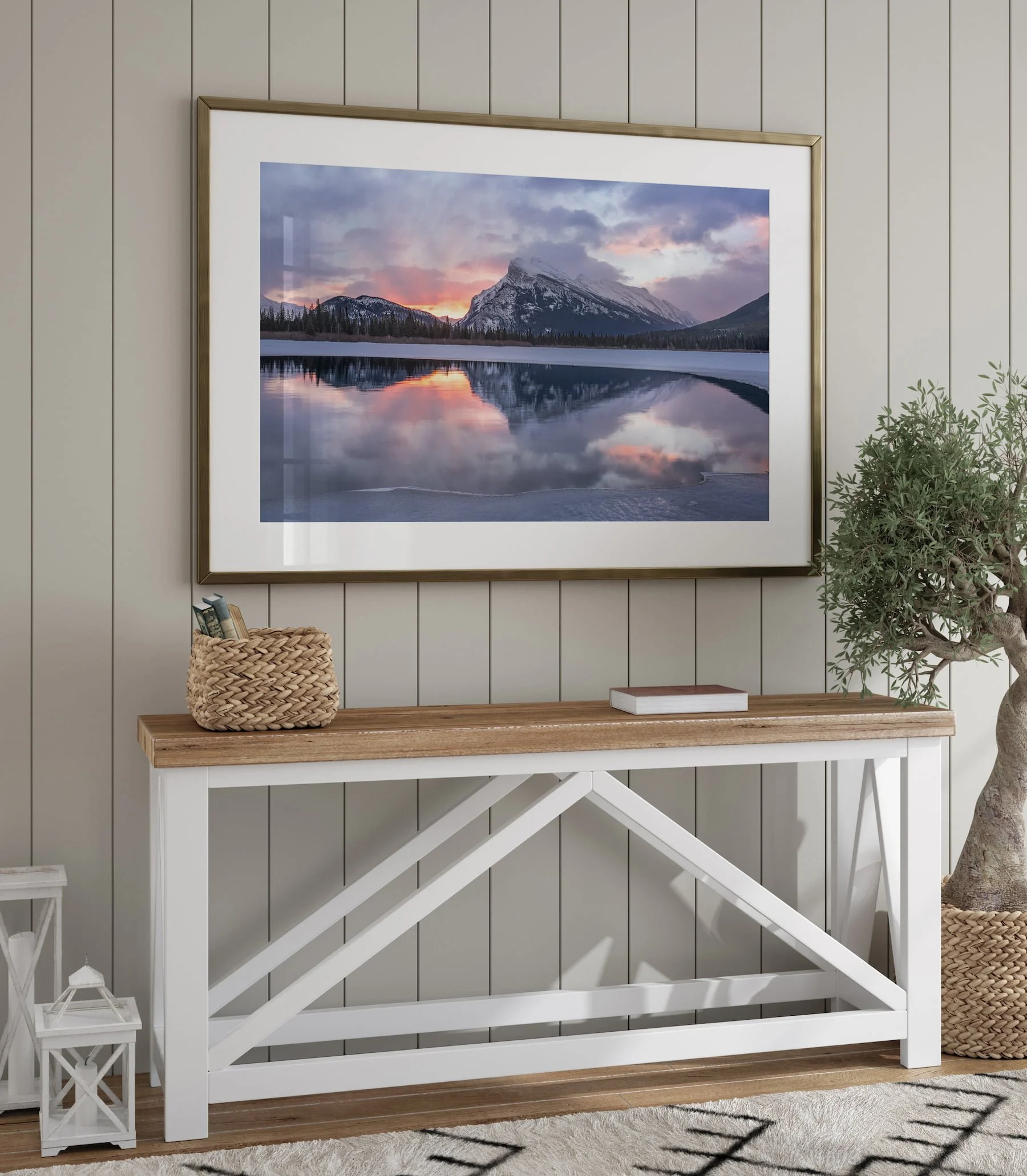 Mount Rundle Reflections landscape fine art print in a gold metal frame with white mat, hung above a rustic farmhouse console table styled with a woven basket and olive tree.