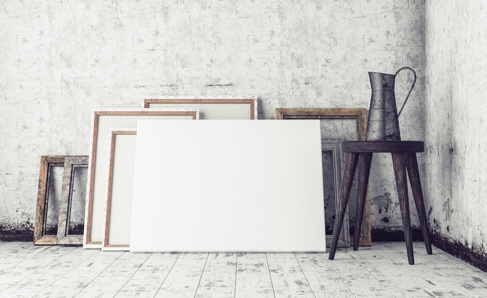 A collection of empty canvas prints and rustic wooden art frames stacked against a weathered white plaster wall next to a dark wood stool