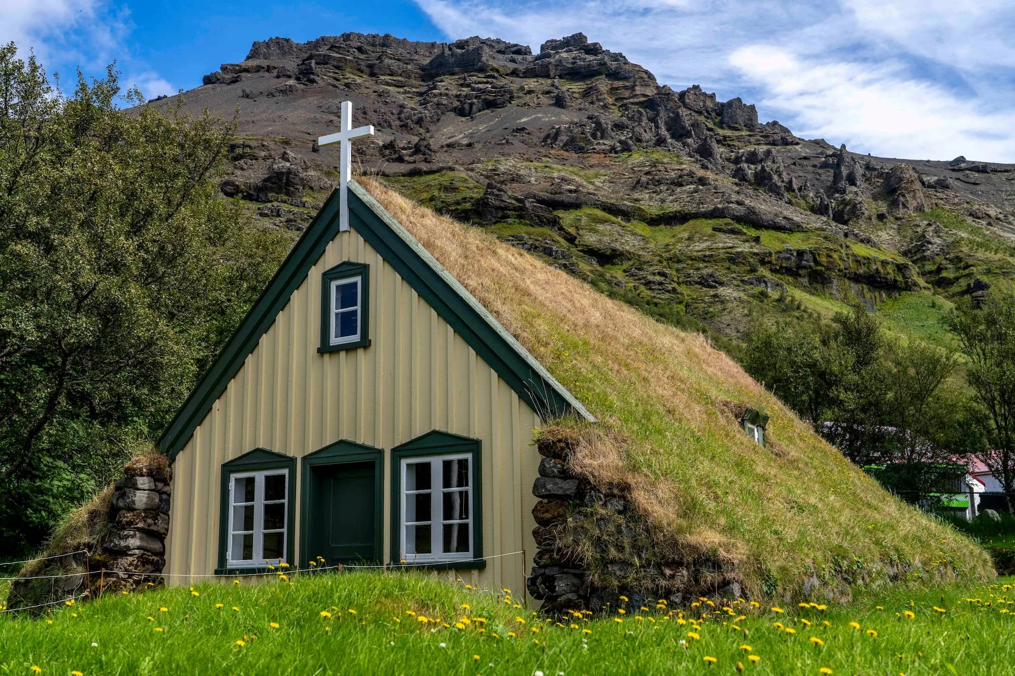 Hofskirkja turf church with its grass-covered roof beneath rocky hills in southeast Iceland.