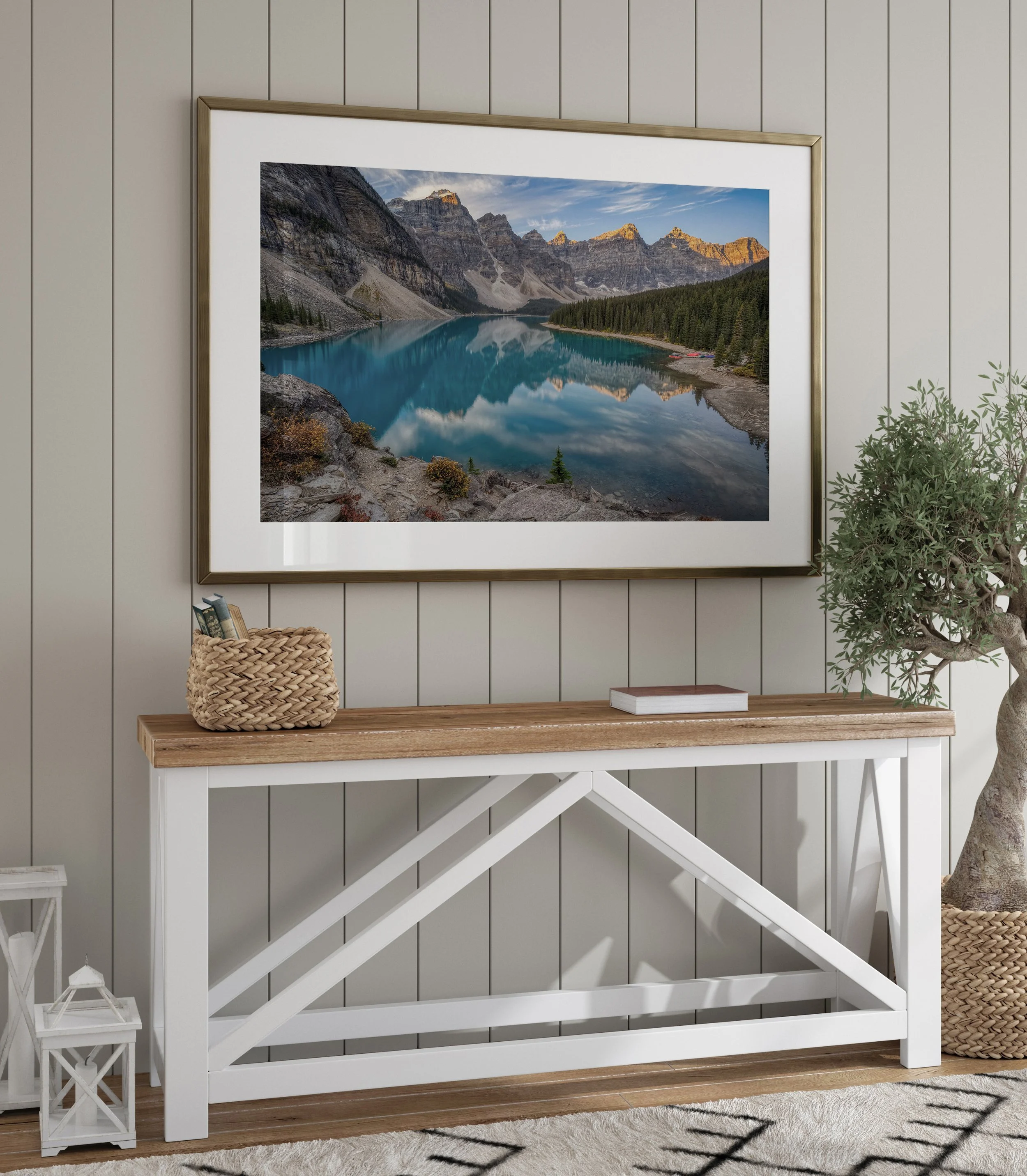 Moraine Lake Sunrise landscape print in a gold metal frame with white mat, hung above a rustic farmhouse console table styled with a woven basket and olive tree.