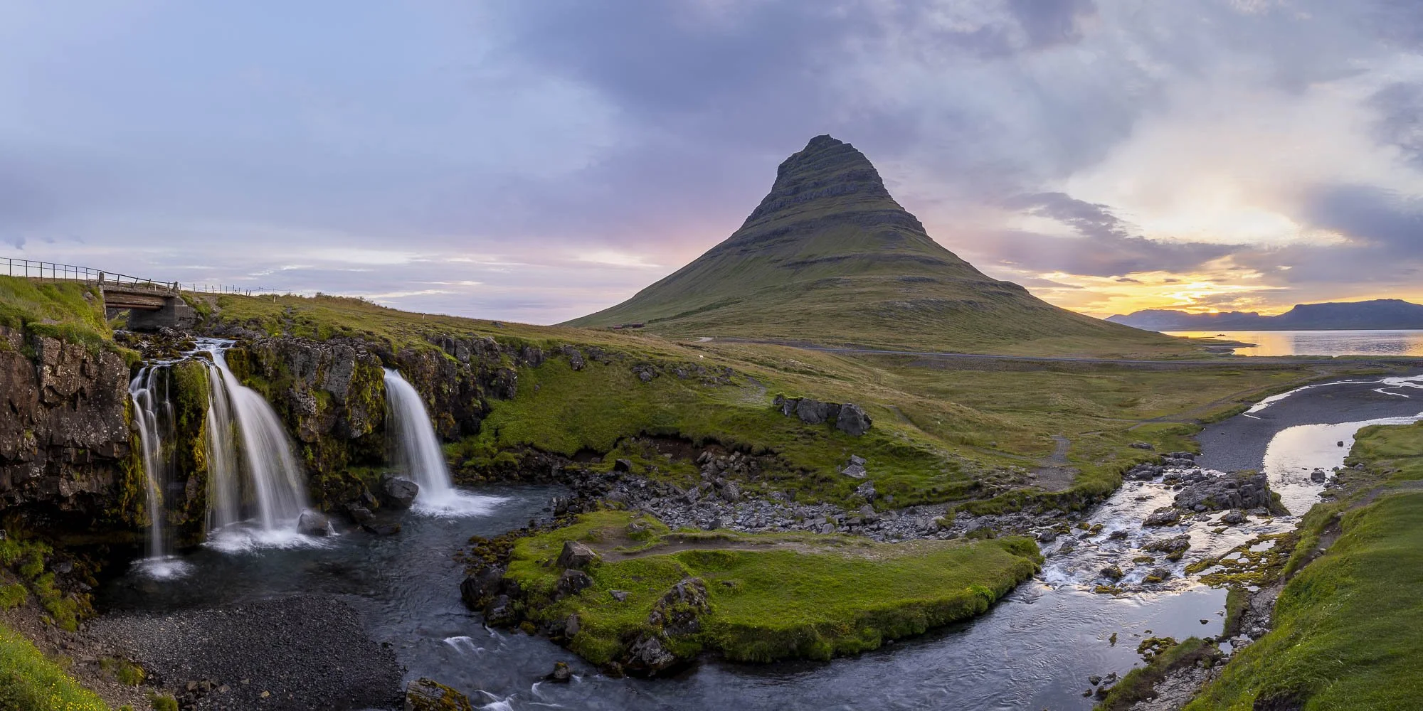 Panoramic view of Kirkjufell, Kirkjufellsfoss and the surrounding river beneath soft early-morning light.