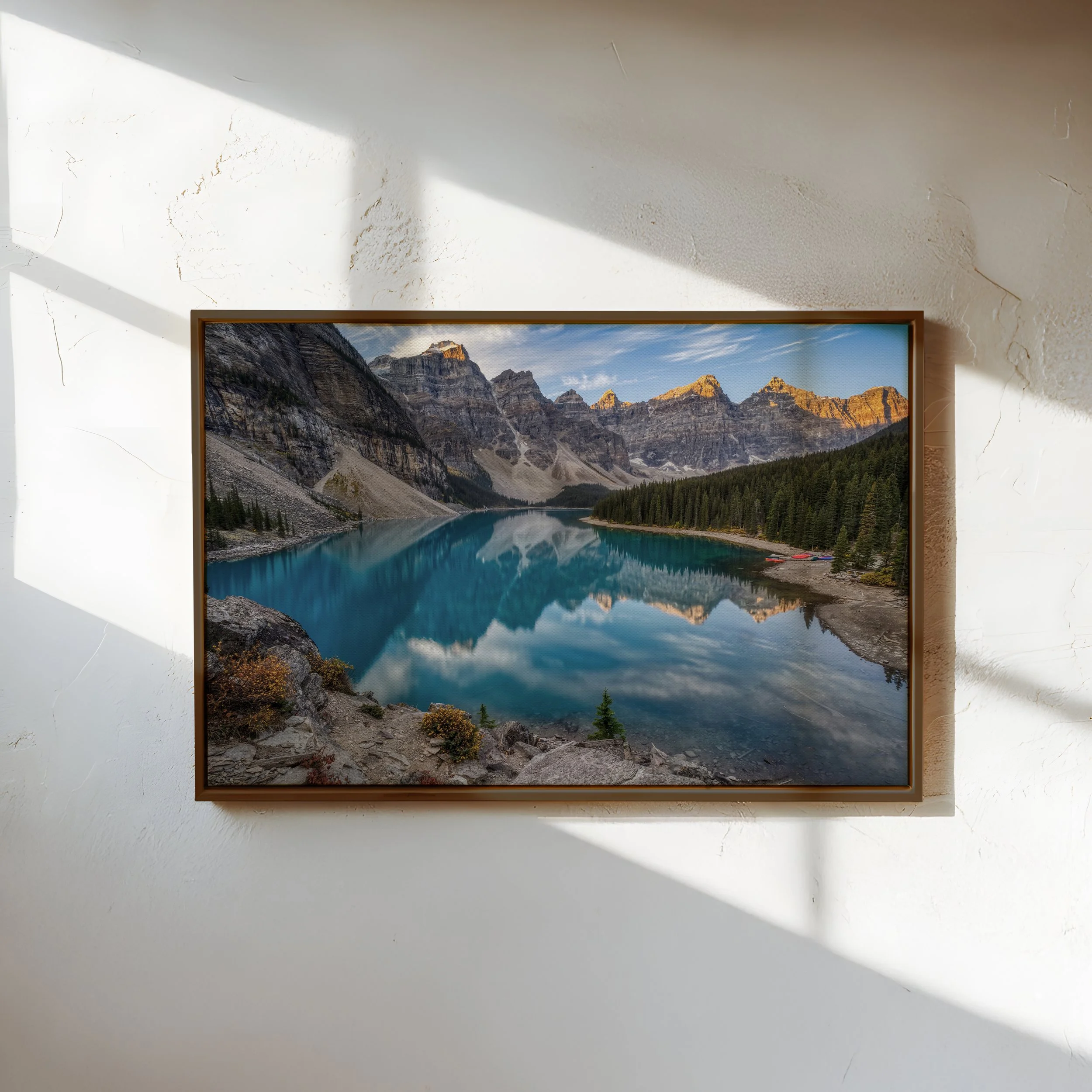 Moraine Lake Sunrise fine art photograph in a walnut floating canvas frame, displayed on a textured white wall with natural window light and shadows.
