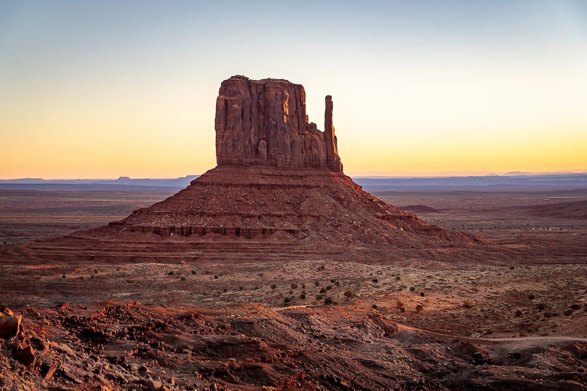 Sunset over a large flat-topped rock formation in a desert landscape with a clear sky.
