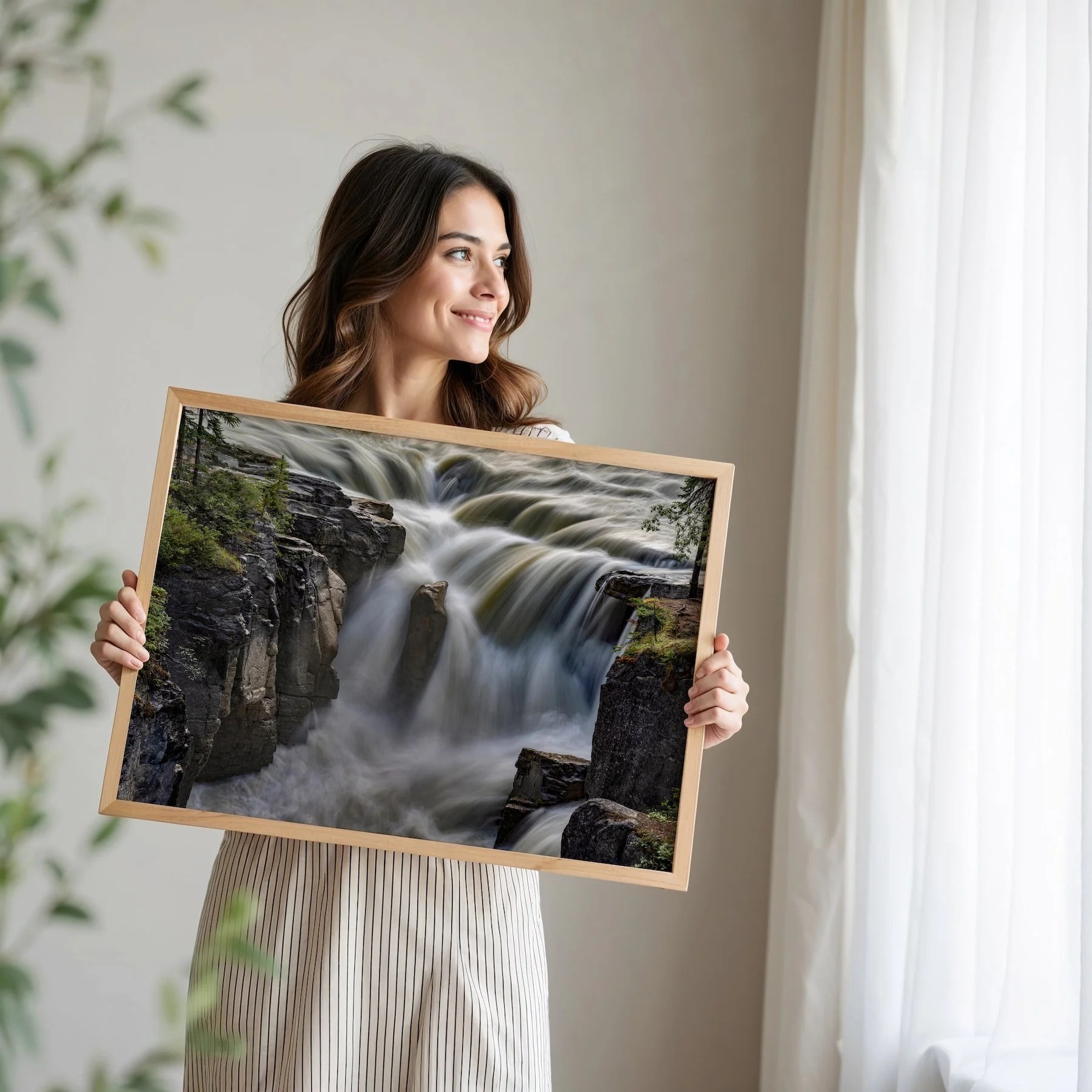 Woman holding framed print of Sunwapta Falls in a bright room.