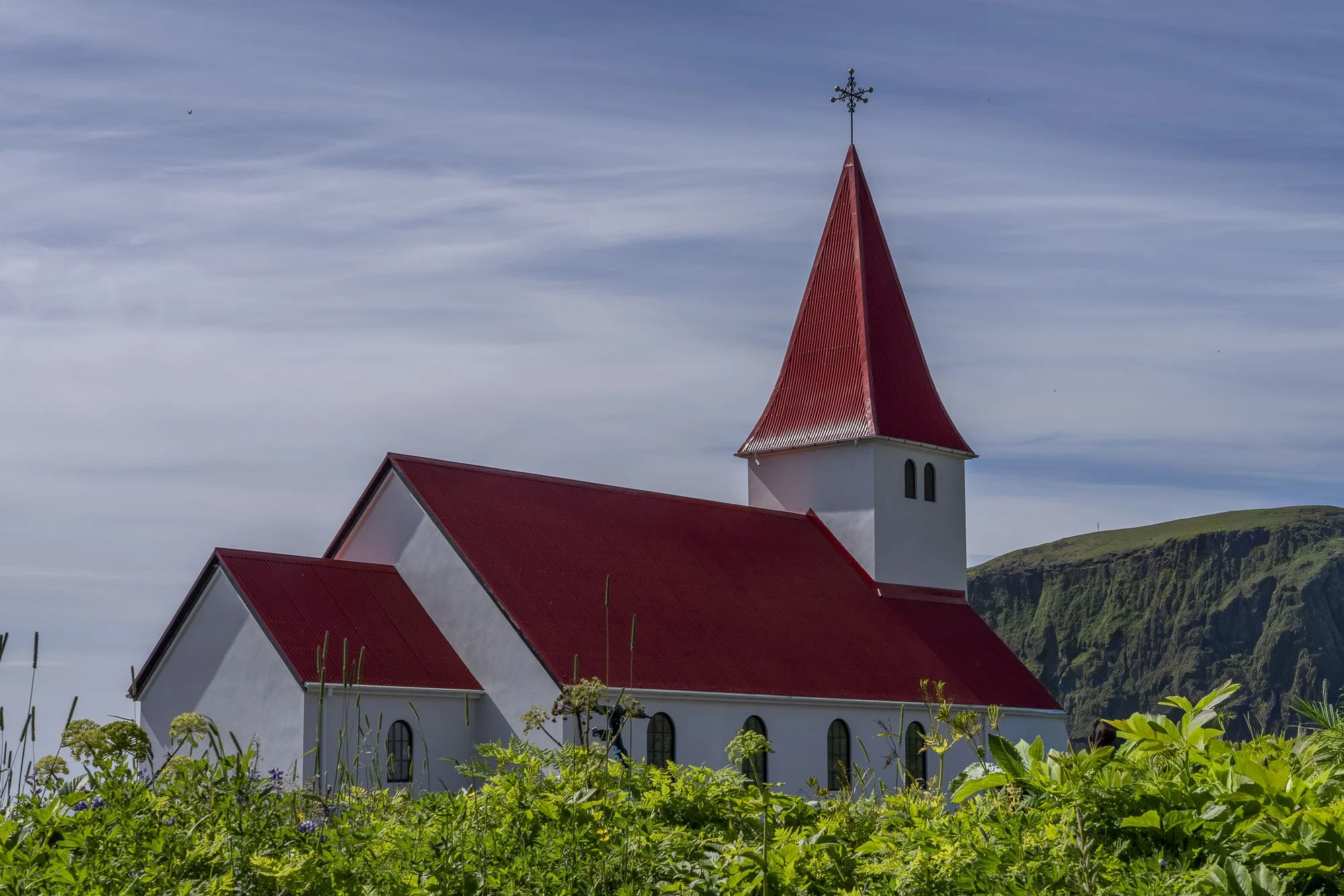 Víkurkirkja church with its red roof above green summer vegetation in Vík, Iceland.