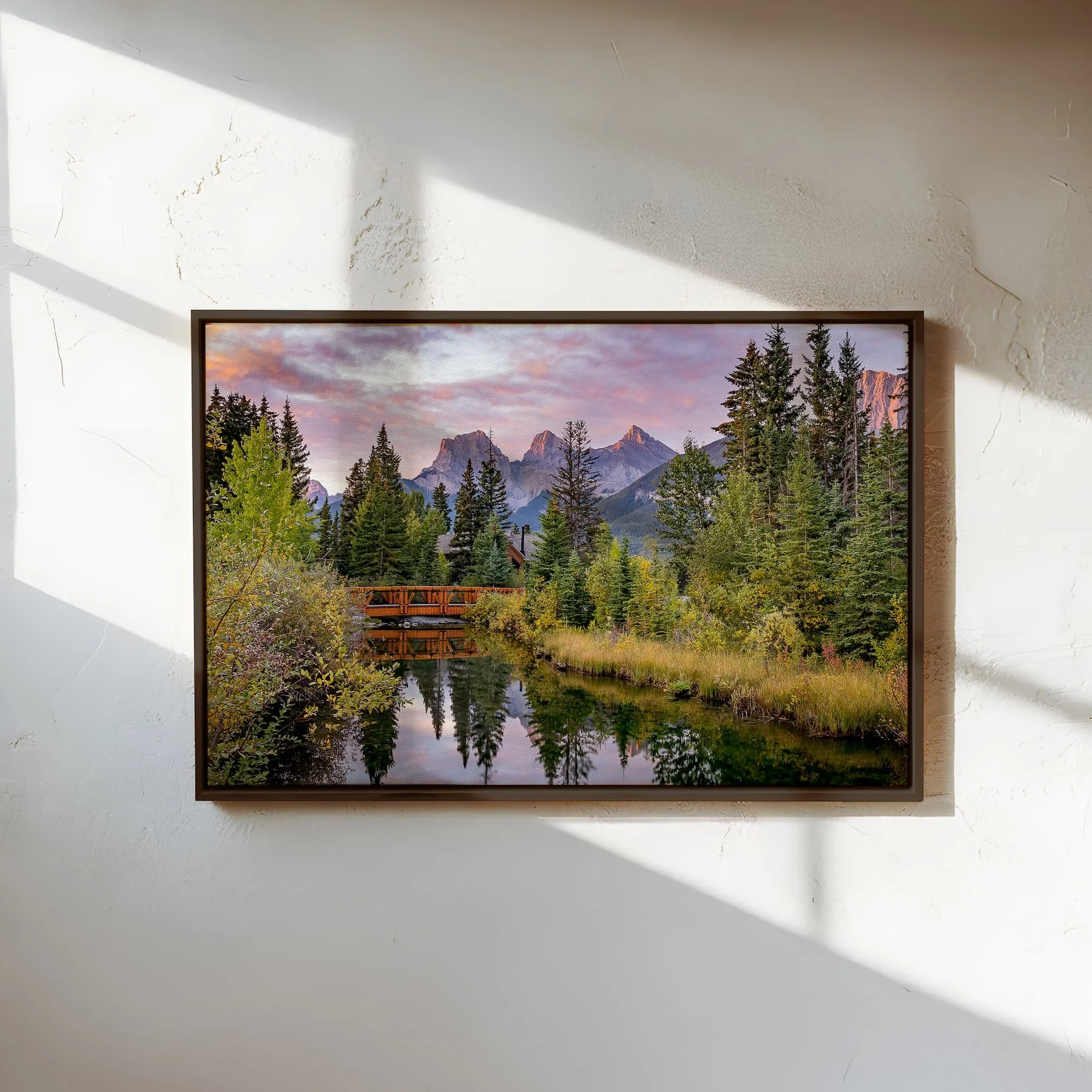 Three Sisters Sunrise fine art print in a slim dark espresso wood frame with white mat, displayed on a clean white wall with soft natural side lighting.