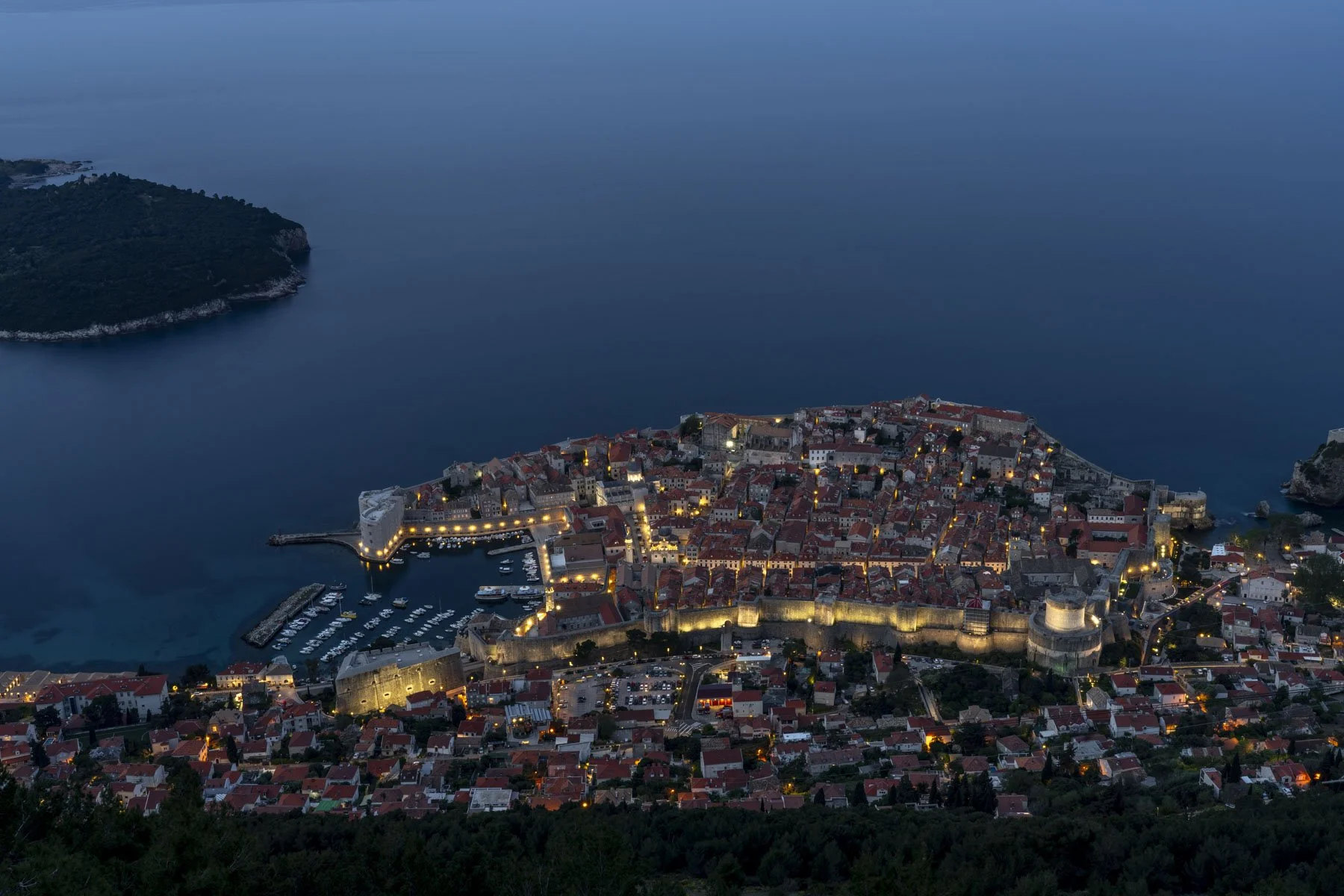 Dubrovnik Old Town illuminated at dusk, viewed from Mt Srd, with city walls, old port, and Lokrum Island.