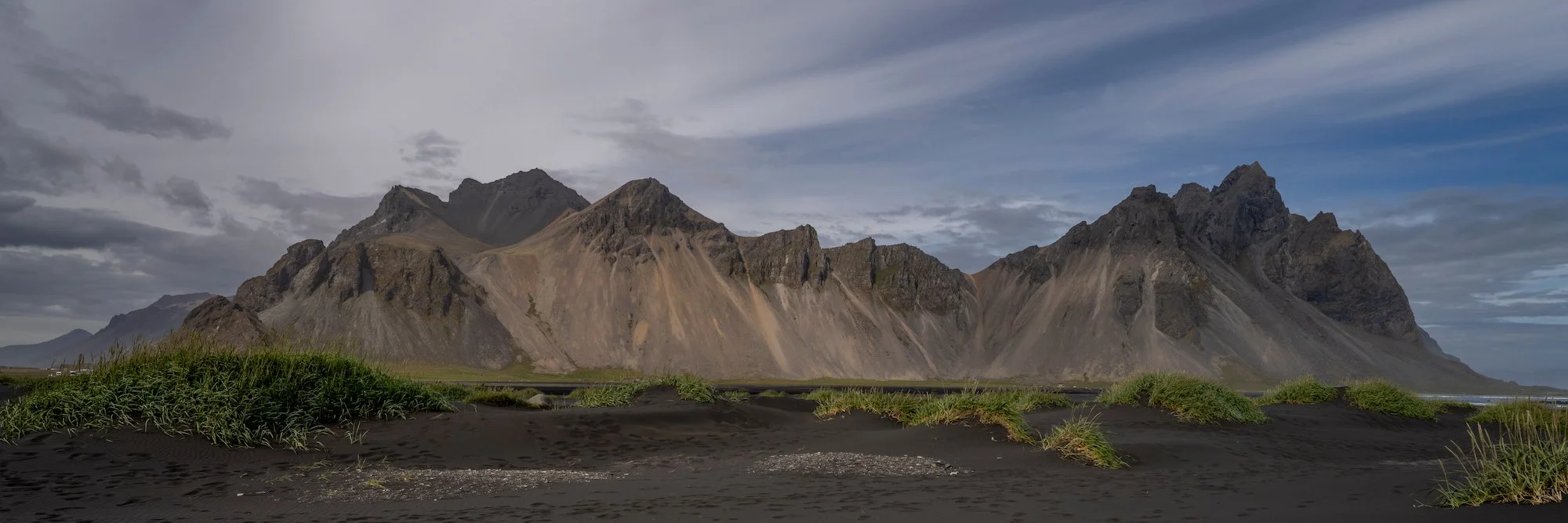 Vestrahorn rising above black sand and grassy dunes beneath a clearing sky at Stokksnes, Iceland.