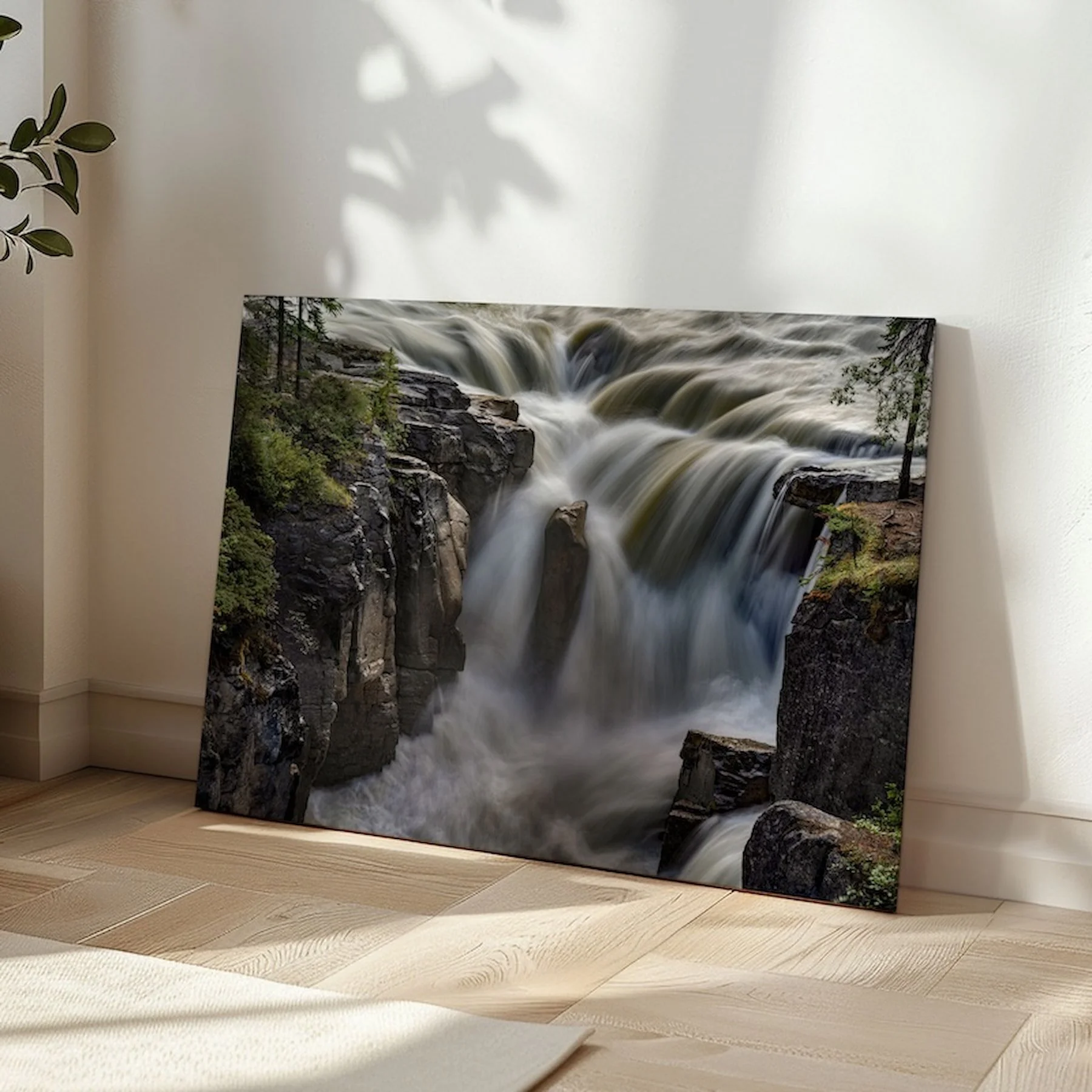 Sunwapta Falls gallery-wrapped canvas print leaning in a sunlit room corner on herringbone hardwood flooring, with soft leaf shadows on the wall beside it.